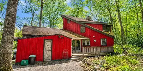 Image 2: A vibrant red siding home nestled among lush trees