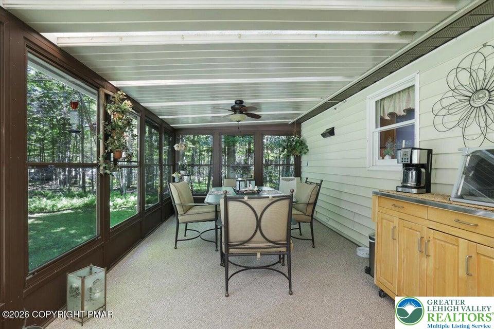 Image 3: A well-lit sunroom overlooks the serene, wooded la