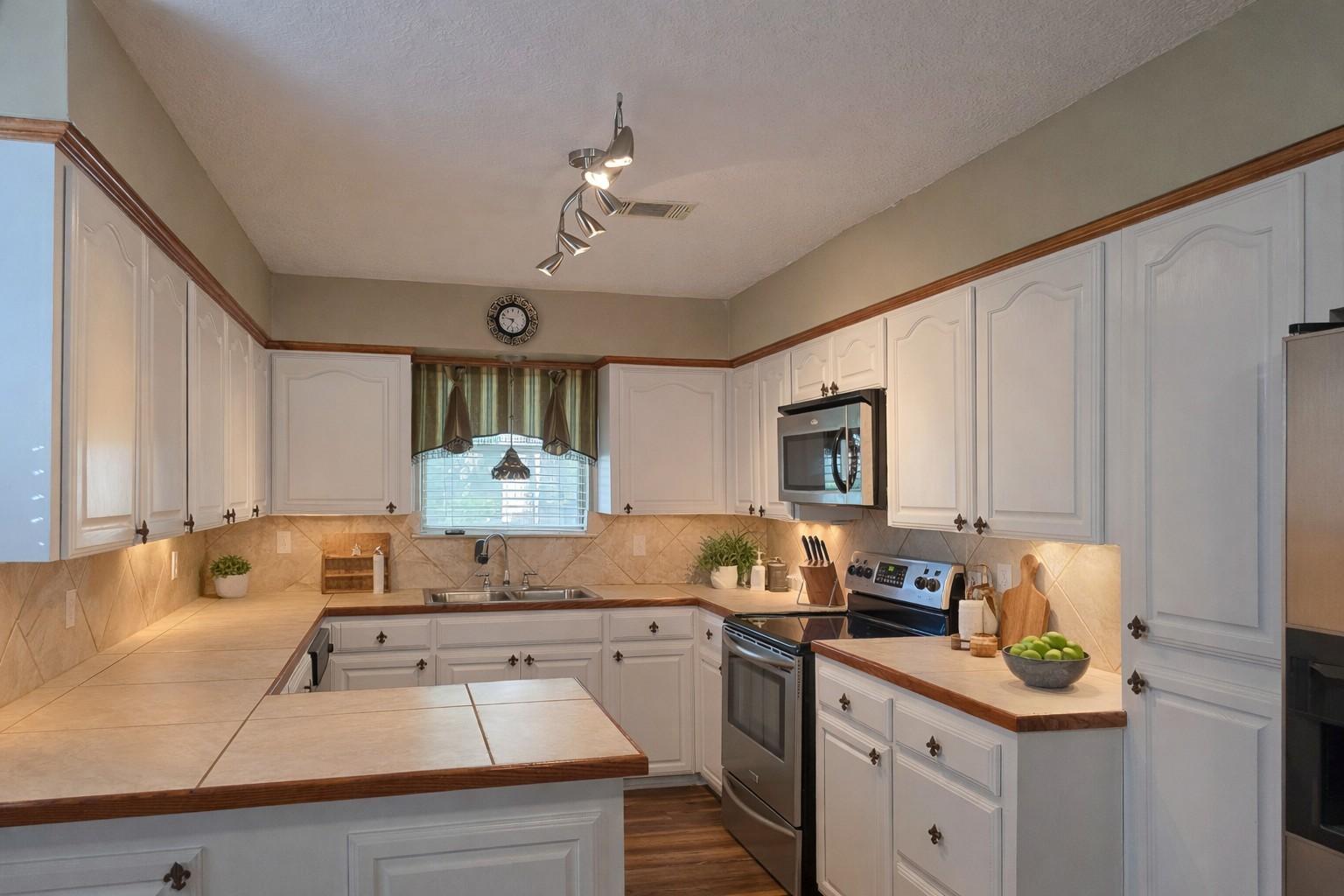 Image 3: This kitchen features ample white cabinetry, stain