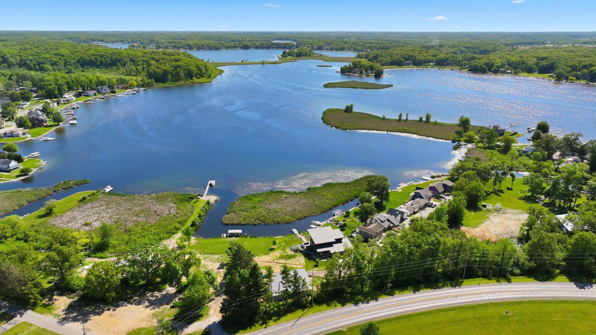 Image 1: Expansive lakefront property featuring a private dock, wetland areas, a paved road, and abundant surrounding greenery, Aerial View Image 1: Expansive lakefront property featuring a private dock, wetland areas, a paved road, and abundant surrounding greenery, Aerial View