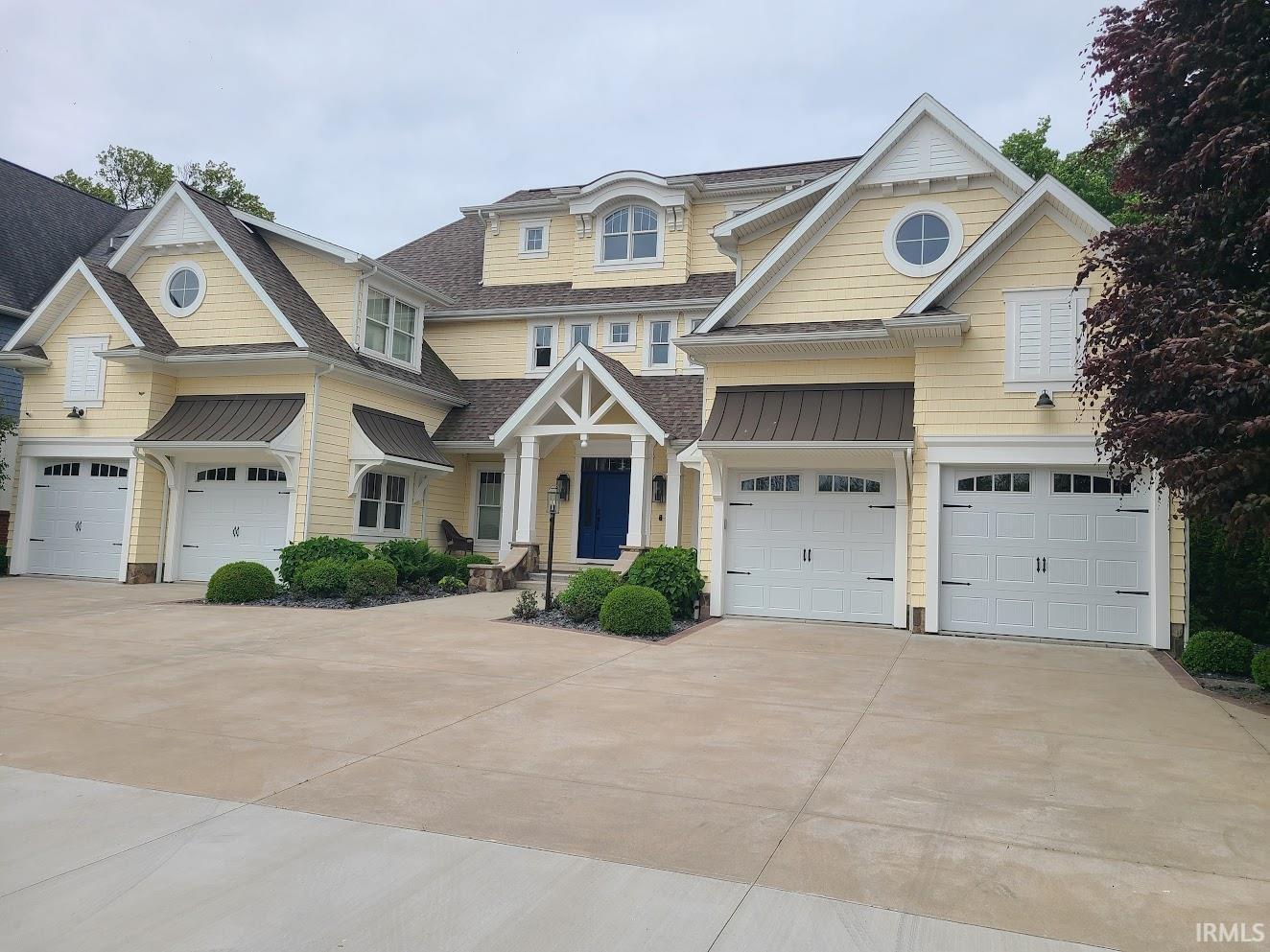 Image 3: Expansive yellow siding residence featuring a prominent blue entry door, multiple gables, and a total of five garage doors, Front Of Structure Image 3: Expansive yellow siding residence featuring a prominent blue entry door, multiple gables, and a total of five garage doors, Front Of Structure