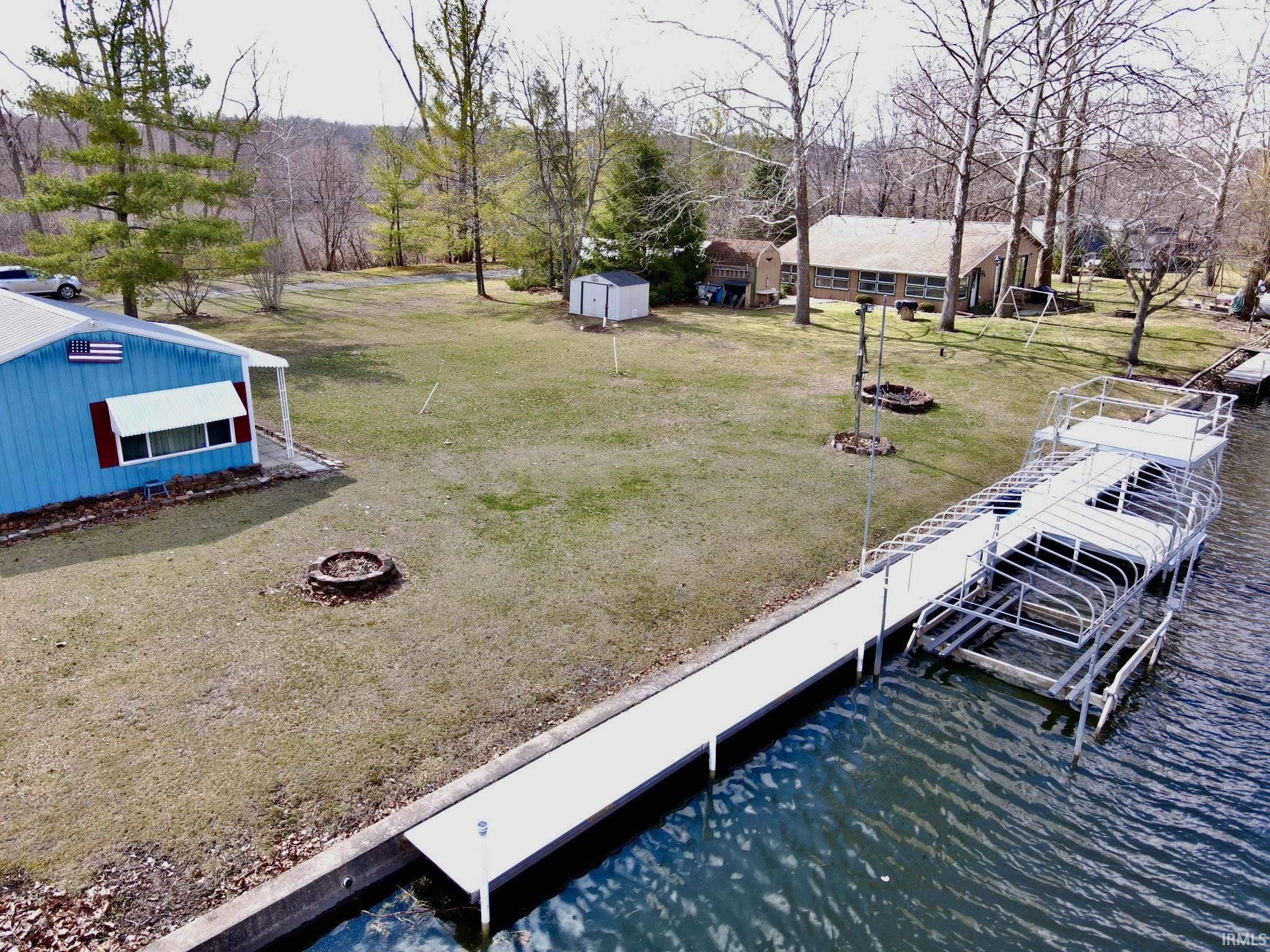 Image 3: View of grassy yard featuring a fire pit, a dock, a water view, and a shed, Yard Image 3: View of grassy yard featuring a fire pit, a dock, a water view, and a shed, Yard
