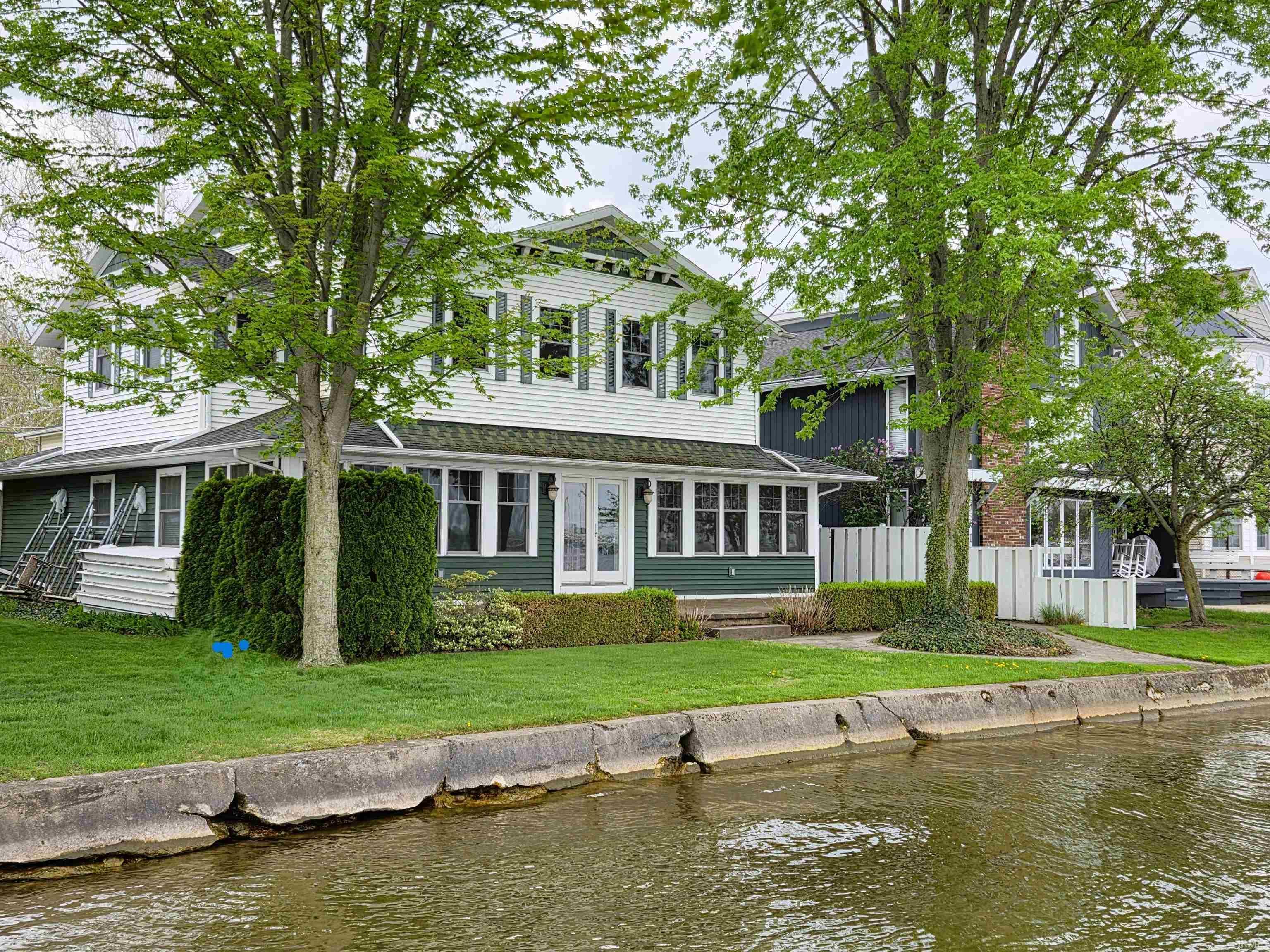 Image 1: Waterfront property featuring a white siding exterior with green accents and an enclosed porch, Back Of Structure Image 1: Waterfront property featuring a white siding exterior with green accents and an enclosed porch, Back Of Structure