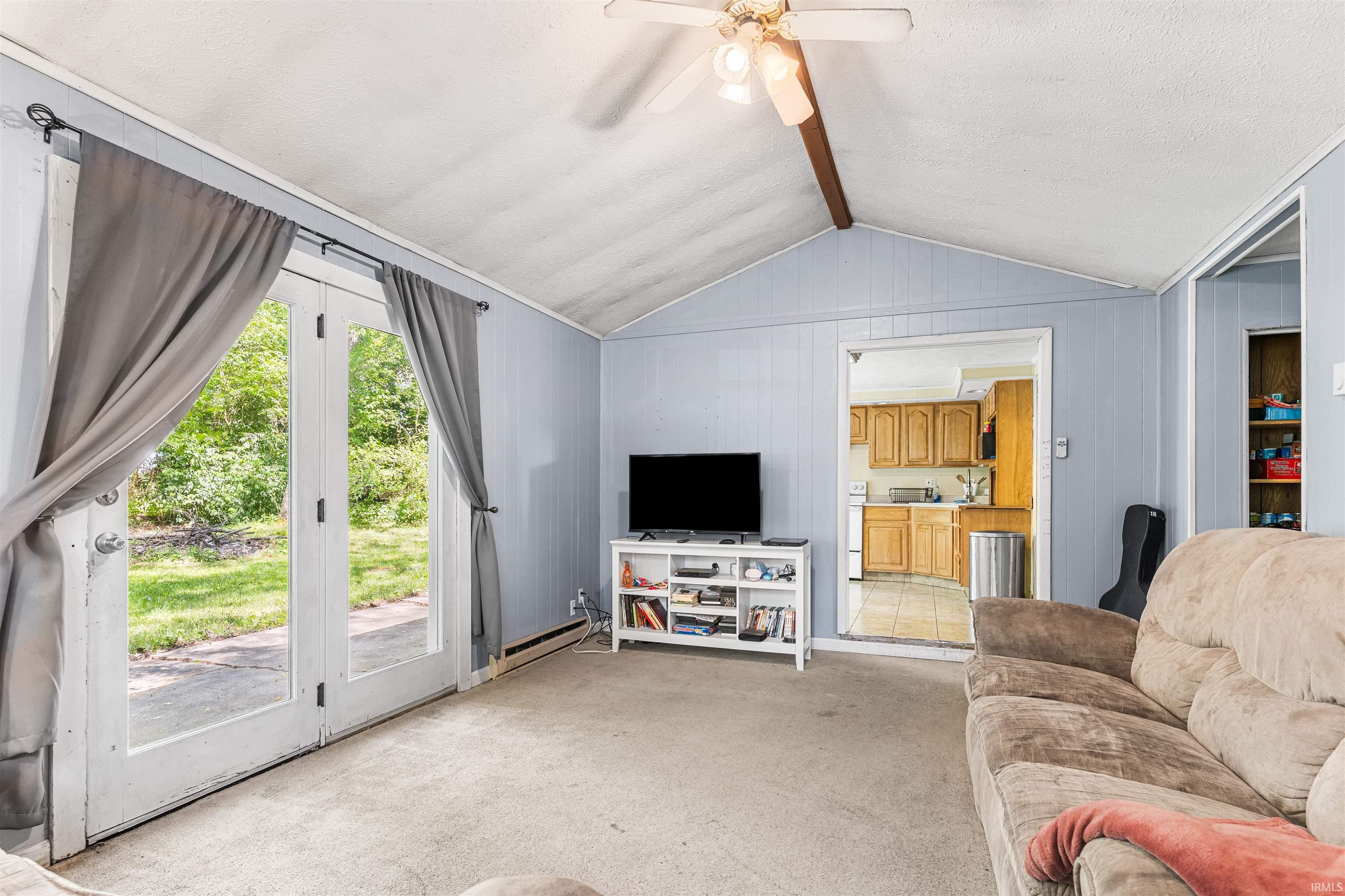 Image 3: Spacious room featuring vaulted ceilings, light blue paneling, a ceiling fan, and double glass-paneled doors leading to the exterior, Living Room Image 3: Spacious room featuring vaulted ceilings, light blue paneling, a ceiling fan, and double glass-paneled doors leading to the exterior, Living Room