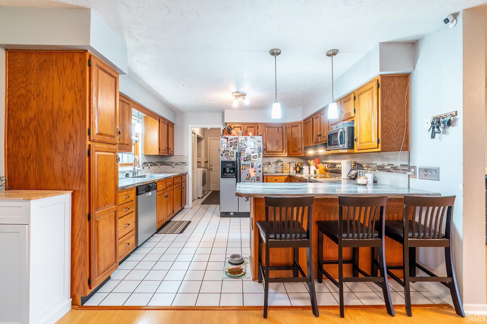 Image 3: Kitchen with a peninsula, wood finish cabinets, stainless steel appliances, a breakfast bar, and light countertops, Kitchen Image 3: Kitchen with a peninsula, wood finish cabinets, stainless steel appliances, a breakfast bar, and light countertops, Kitchen