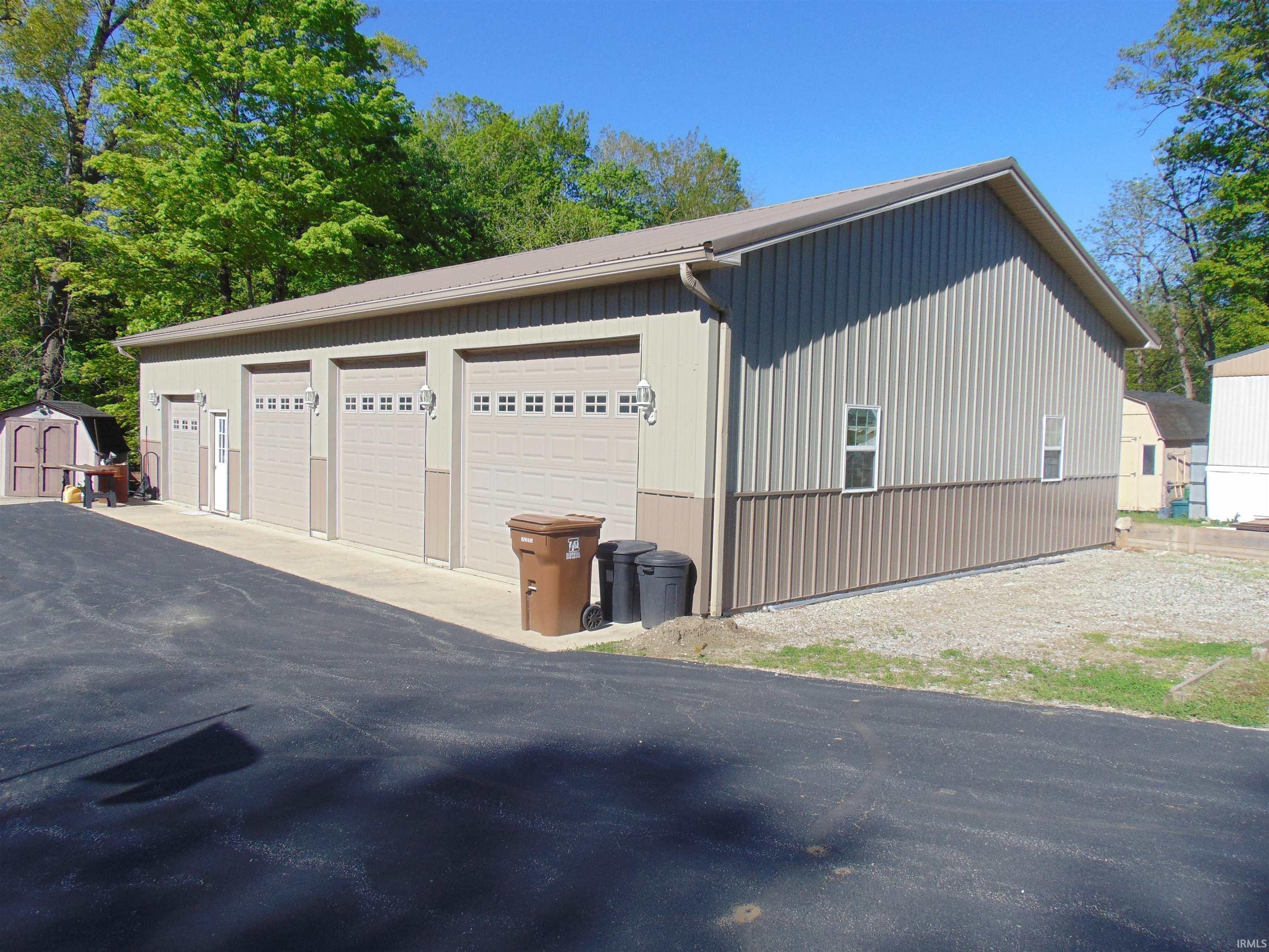 Image 1: Multi-bay garage featuring four beige garage doors with window inserts, a separate entry door, and a light-colored metal roof, Garage Image 1: Multi-bay garage featuring four beige garage doors with window inserts, a separate entry door, and a light-colored metal roof, Garage