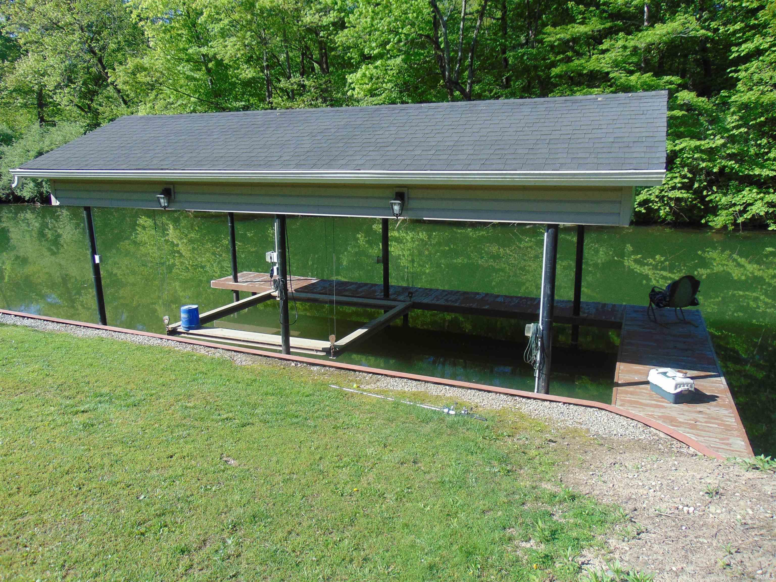 Image 3: Covered boat dock featuring a dark shingle roof, light-colored siding, and a boat lift, Dock Image 3: Covered boat dock featuring a dark shingle roof, light-colored siding, and a boat lift, Dock