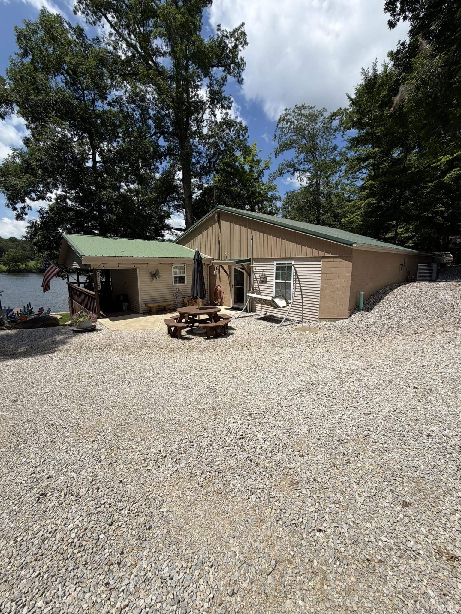 Image 0: Waterfront property featuring a gravel parking area, a covered patio, and a metal roof, Front Of Structure Image 0: Waterfront property featuring a gravel parking area, a covered patio, and a metal roof, Front Of Structure