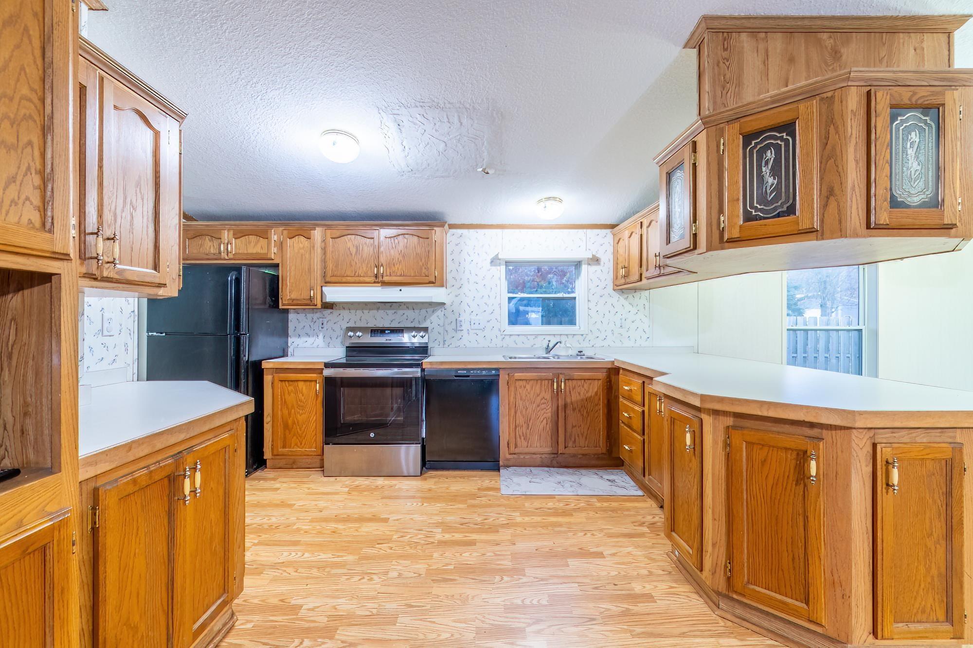 Image 2: Kitchen featuring brown cabinetry, black appliances, light countertops, light wood-style flooring, and a textured ceiling, Kitchen Image 2: Kitchen featuring brown cabinetry, black appliances, light countertops, light wood-style flooring, and a textured ceiling, Kitchen