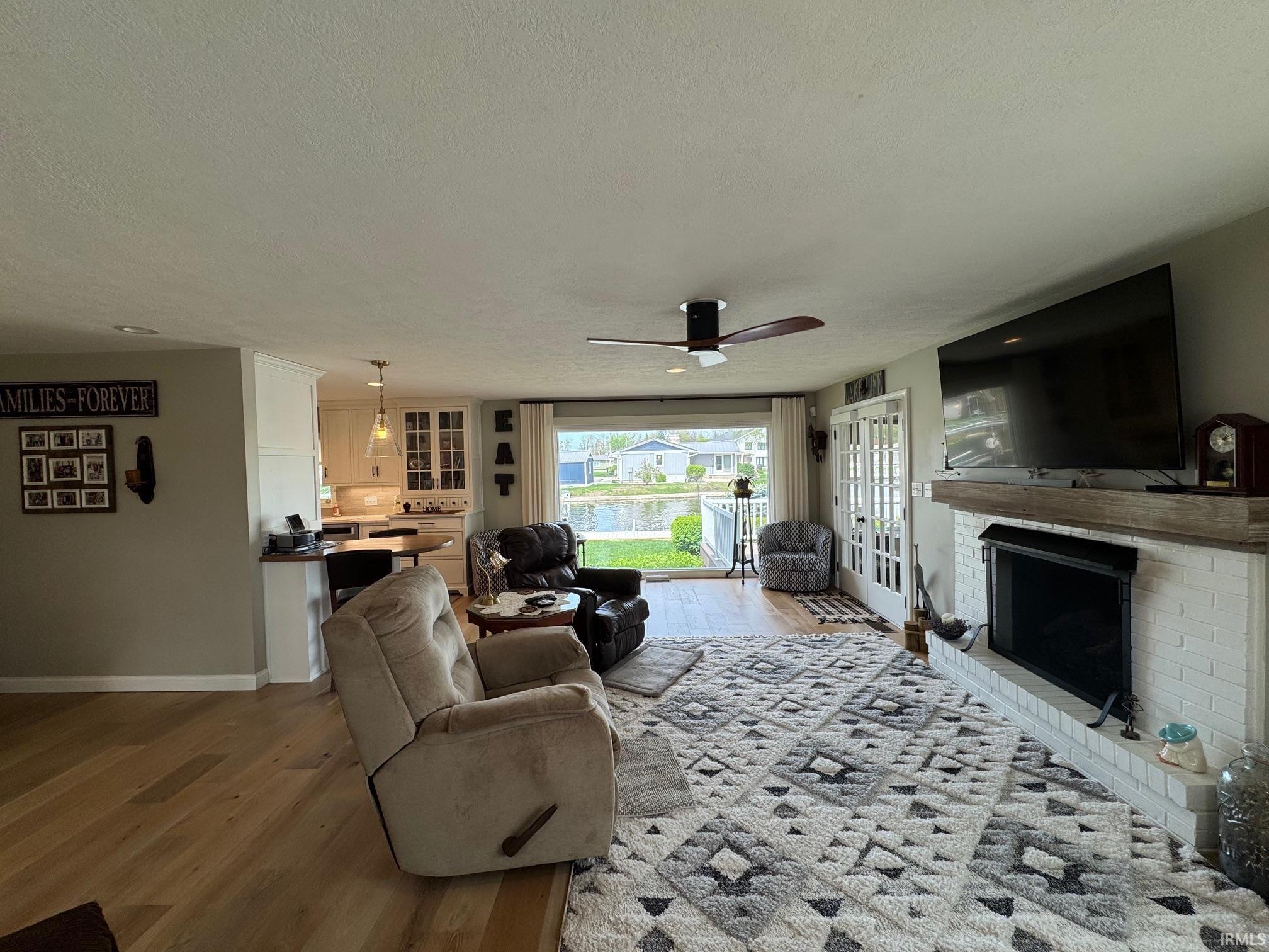 Image 1: Living area with light wood finished floors, a ceiling fan, a fireplace, and a textured ceiling, Living Room