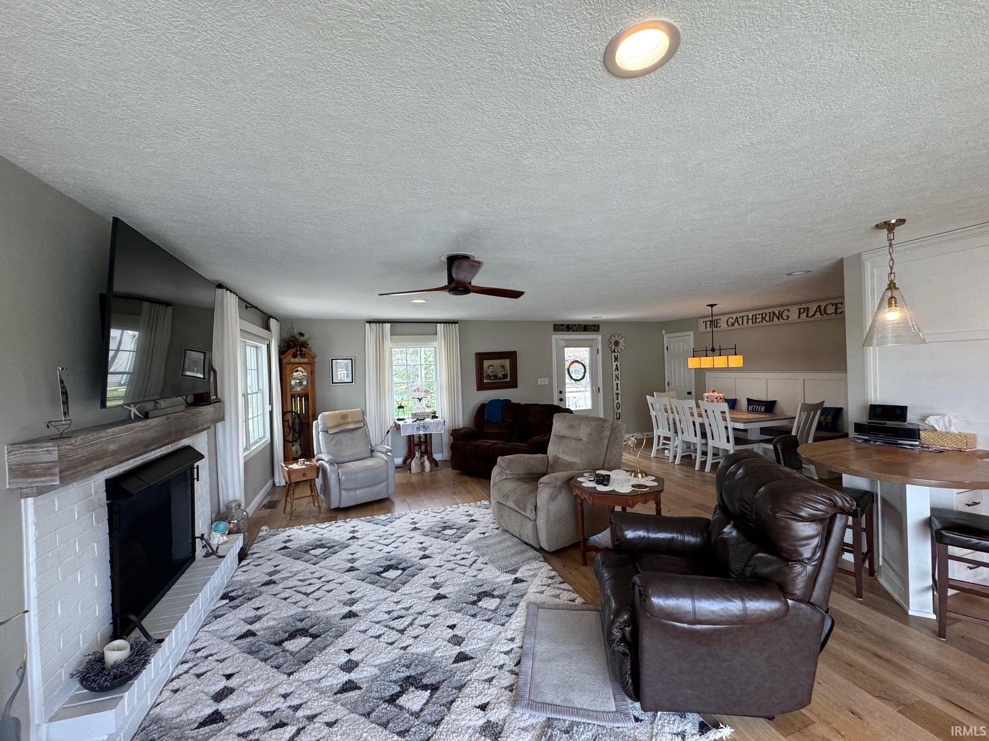Image 3: Living area featuring a brick fireplace, light wood-style floors, ceiling fan, and a textured ceiling, Living Room