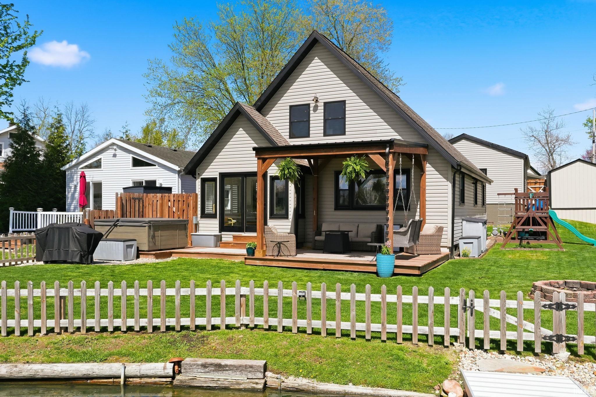 Image 2: Back of property with a hot tub, a wooden deck, a fenced backyard, and a playground, Back Of Structure