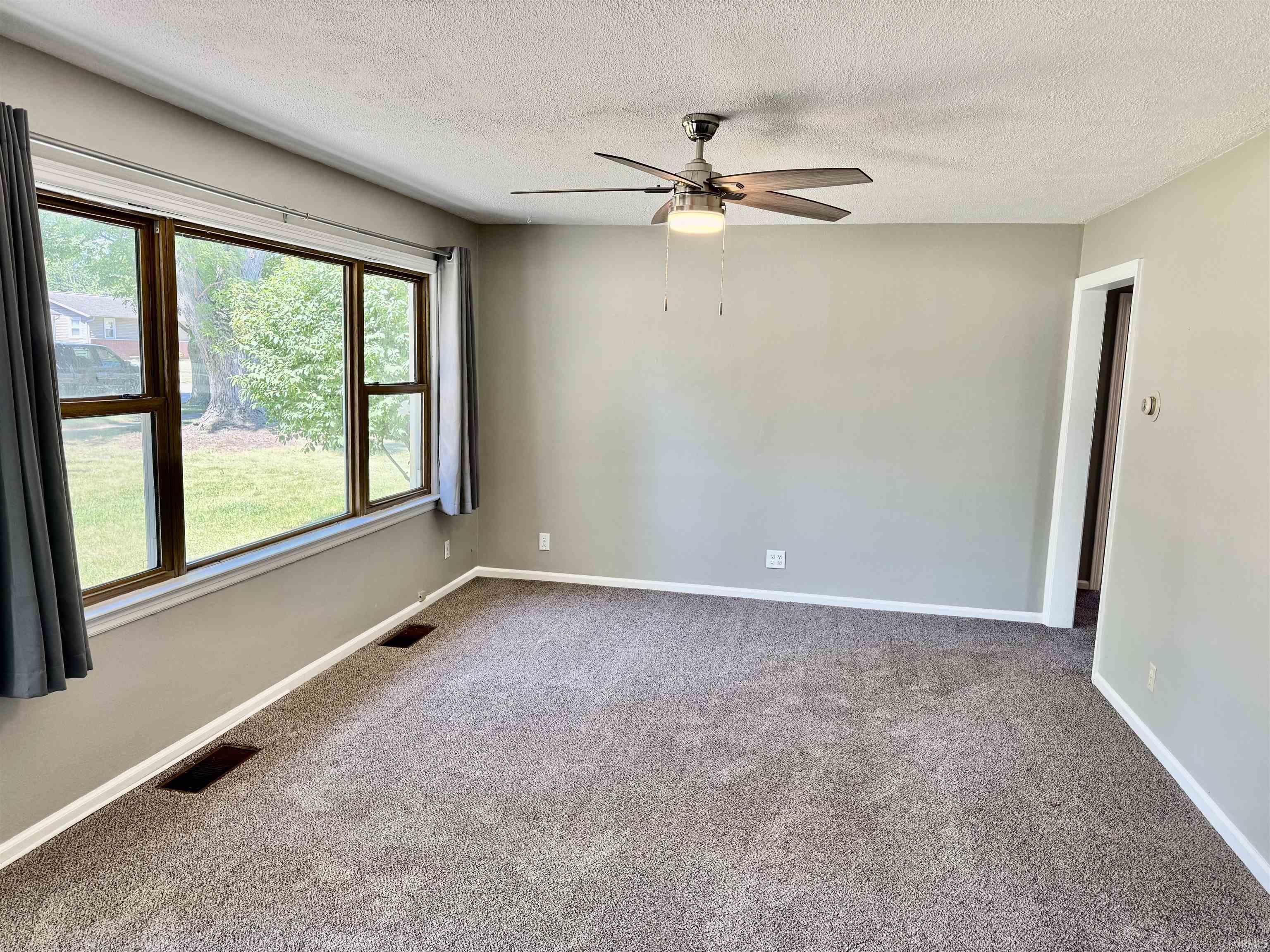 Image 3: Carpeted interior space featuring neutral wall paint, white trim, a ceiling fan with light fixture, and multiple windows with dark frames, Entrance Foyer Image 3: Carpeted interior space featuring neutral wall paint, white trim, a ceiling fan with light fixture, and multiple windows with dark frames, Entrance Foyer