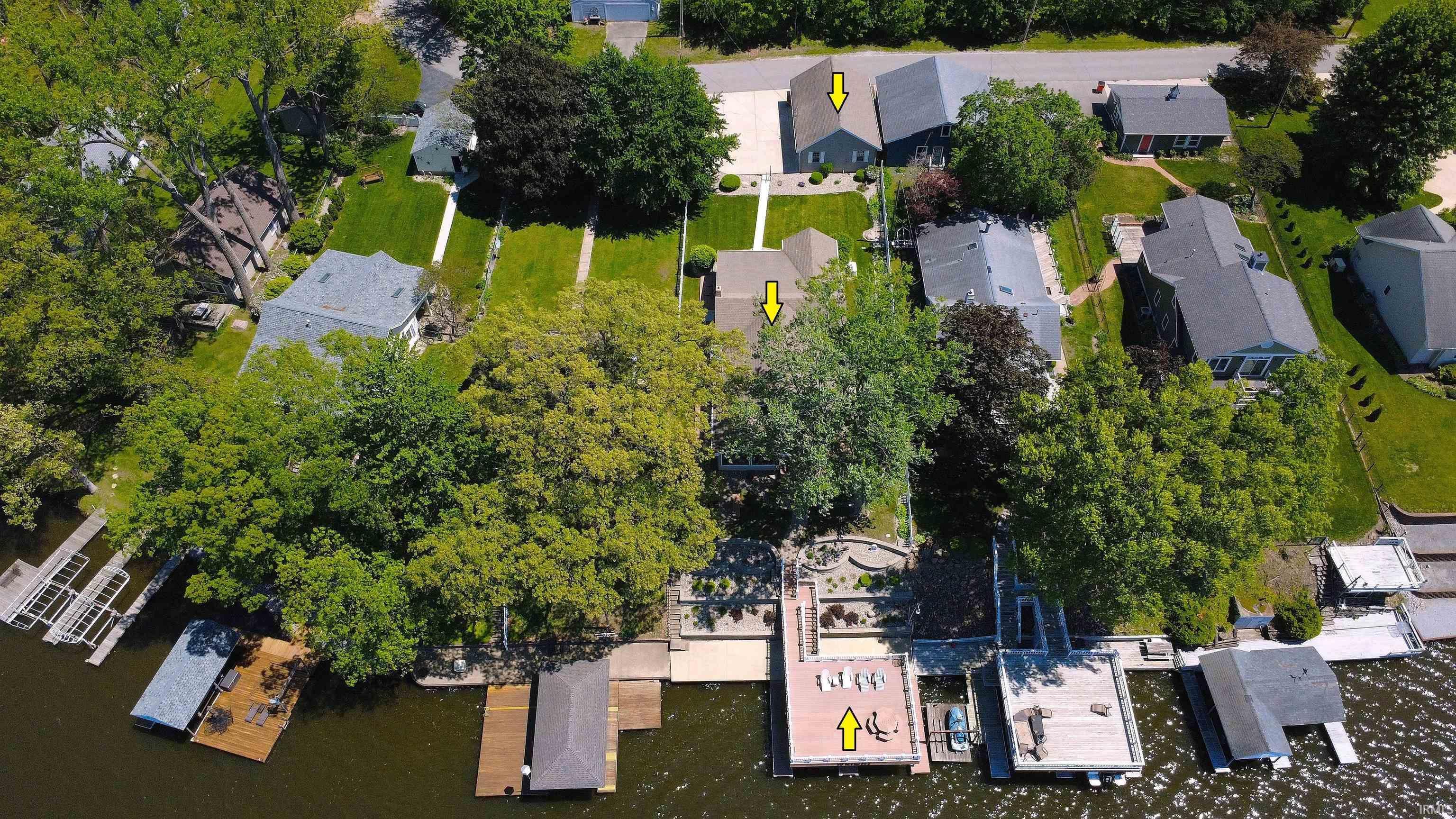 Image 3: Waterfront property featuring multiple boat docks, a large deck, established trees, and a spacious green lawn, Aerial View