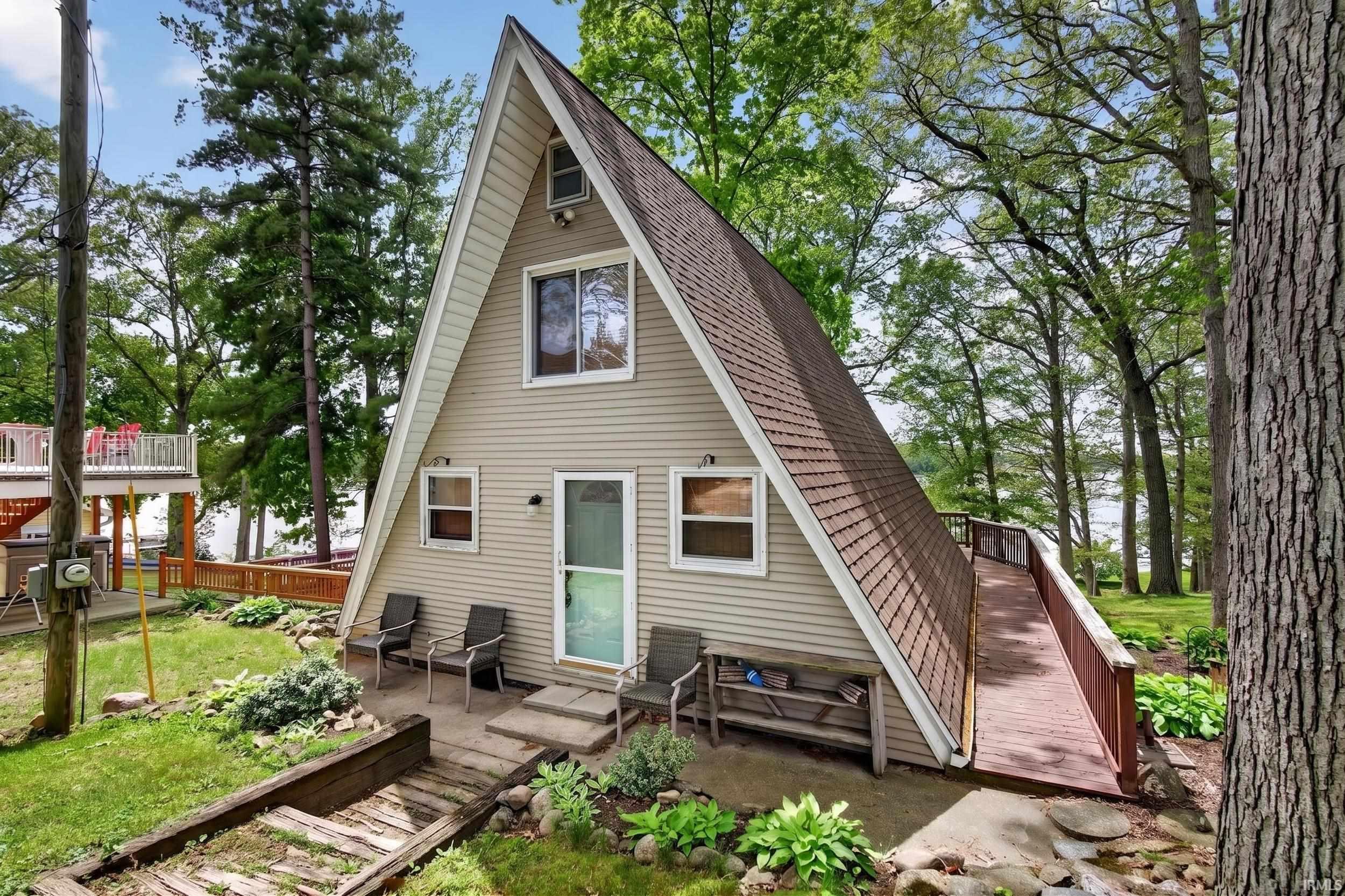 Image 1: A-frame structure featuring light-colored siding and a contrasting brown shingle roof, Street side Image 1: A-frame structure featuring light-colored siding and a contrasting brown shingle roof, Street side