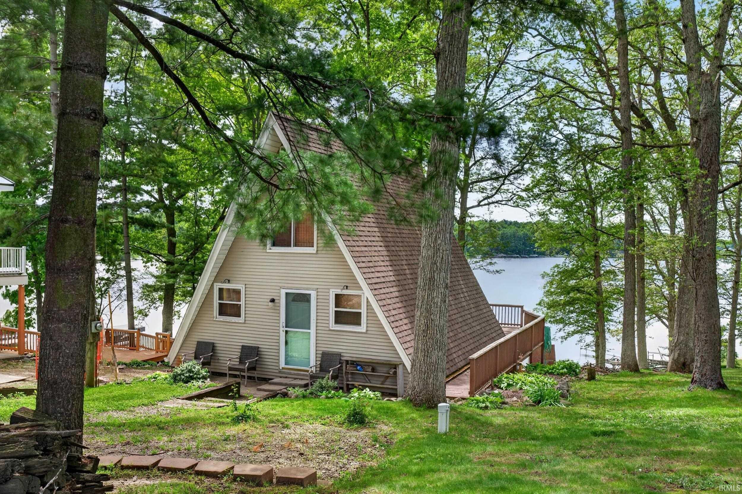 Image 2: A-frame residence featuring a shingle roof and light-colored siding, surrounded by mature trees, Street side Image 2: A-frame residence featuring a shingle roof and light-colored siding, surrounded by mature trees, Street side