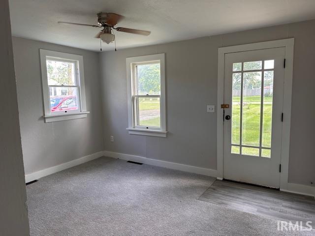 Image 2: Room featuring light gray walls, two sash windows with white trim, a multi-pane glass panel door, gray carpet flooring, and a ceiling fan, Entry Image 2: Room featuring light gray walls, two sash windows with white trim, a multi-pane glass panel door, gray carpet flooring, and a ceiling fan, Entry