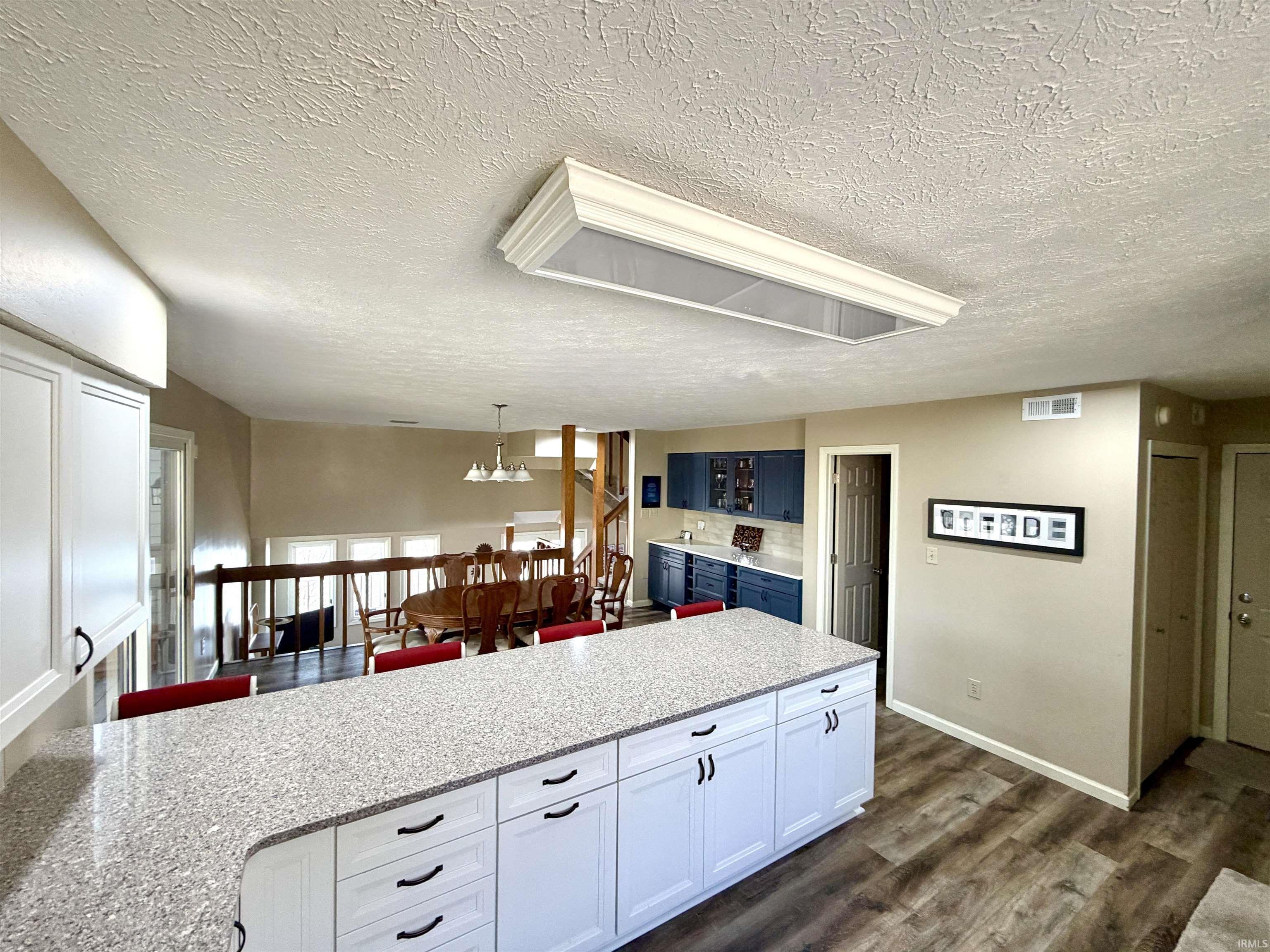 Image 3: Kitchen featuring a textured ceiling, white cabinetry, dark wood finished floors, a peninsula, and hanging lights, Kitchen