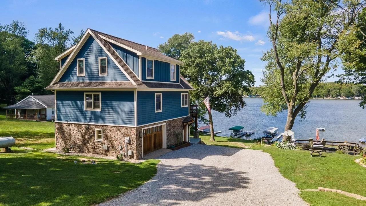 Image 0: Waterfront property featuring a multi-level home with blue siding, a stone foundation, and a pitched roof, Side Of Structure