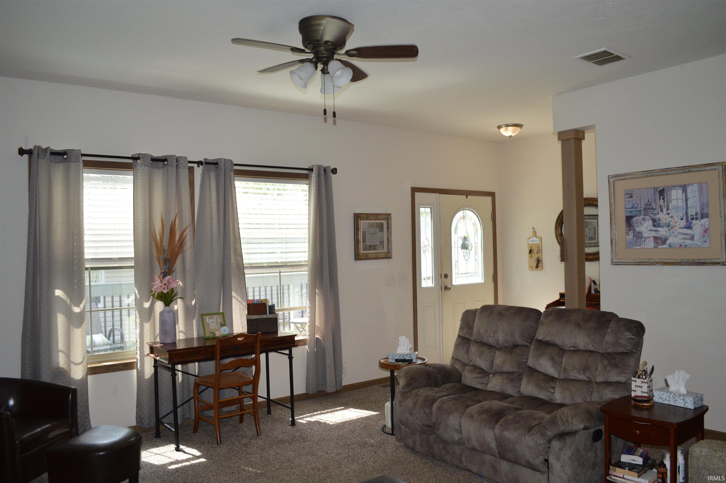 Image 3: Living area featuring a ceiling fan with light fixture, multiple windows with blinds and curtain rods, and a white entry door with decorative glass, Living Room Image 3: Living area featuring a ceiling fan with light fixture, multiple windows with blinds and curtain rods, and a white entry door with decorative glass, Living Room