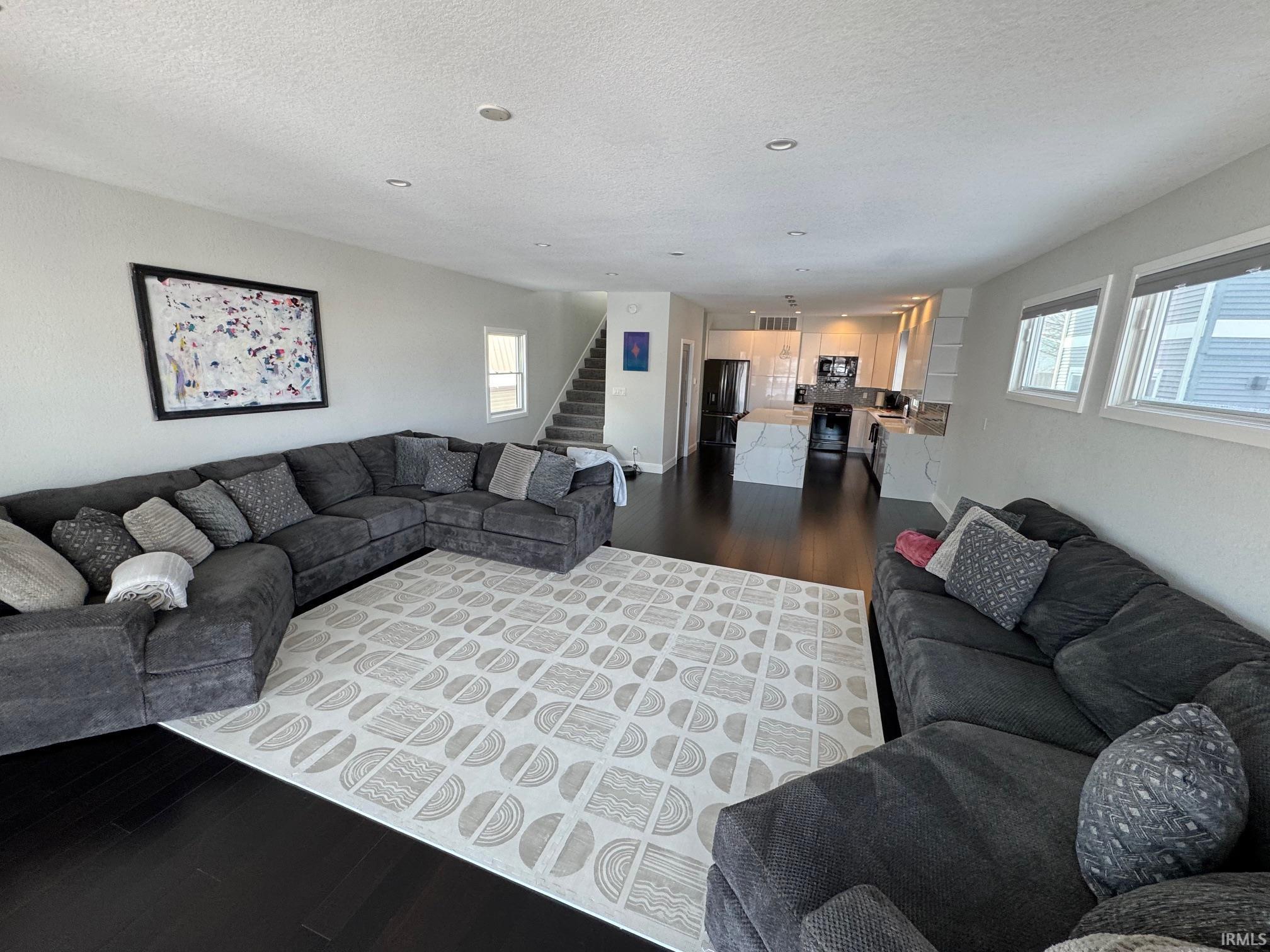 Image 3: Living area with dark wood-style floors, plenty of natural light, stairs, and a textured ceiling, Living Room