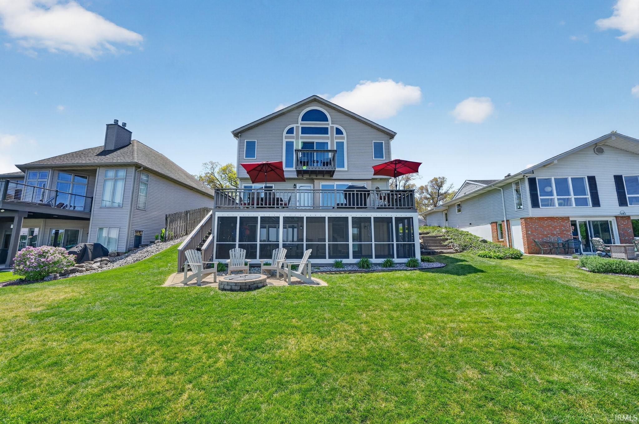 Image 0: exterior with a spacious green lawn, featuring a screened-in patio, an upper-level deck, and an integrated fire pit area, lakeside