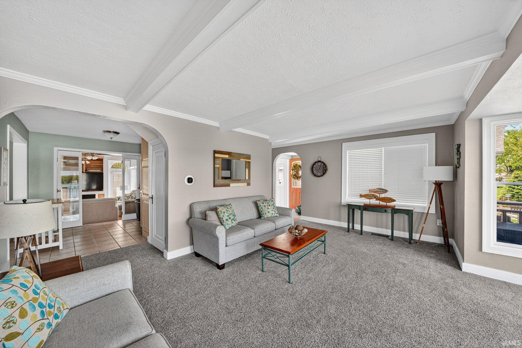 Image 3: Living room featuring a neutral color palette, ceiling beams, arched doorways, a large window with white blinds, and gray carpeting, Living Room
