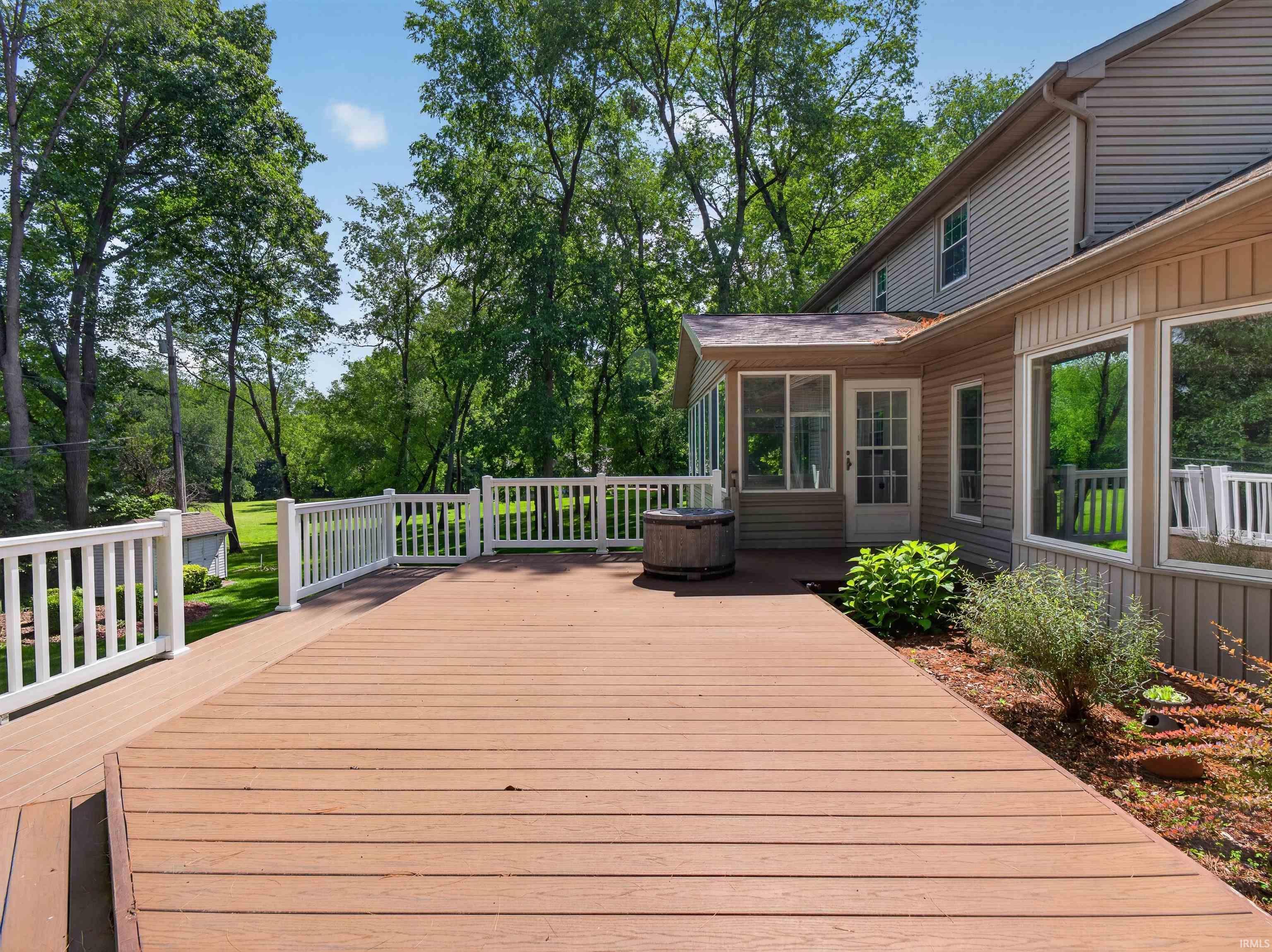 Image 3: Expansive wood-finish deck with white railings, a screened-in porch, and a private rear yard with mature trees, Deck