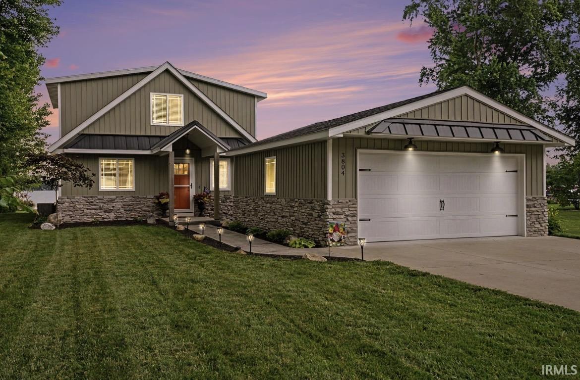 Image 2: Contemporary residence featuring vertical board and batten siding, stone veneer accents, an attached garage with overhead lighting, a covered entry porch, and a concrete walkway with pathway lighting Image 2: Contemporary residence featuring vertical board and batten siding, stone veneer accents, an attached garage with overhead lighting, a covered entry porch, and a concrete walkway with pathway lighting