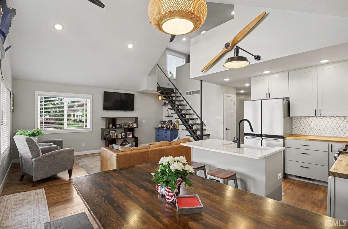 Image 4: Open-concept living space featuring a vaulted ceiling with recessed lighting, wood-finish flooring, and a modern kitchen with a white quartz island, light gray cabinetry, and a diamond-patterned tile backsplash Image 4: Open-concept living space featuring a vaulted ceiling with recessed lighting, wood-finish flooring, and a modern kitchen with a white quartz island, light gray cabinetry, and a diamond-patterned tile backsplash