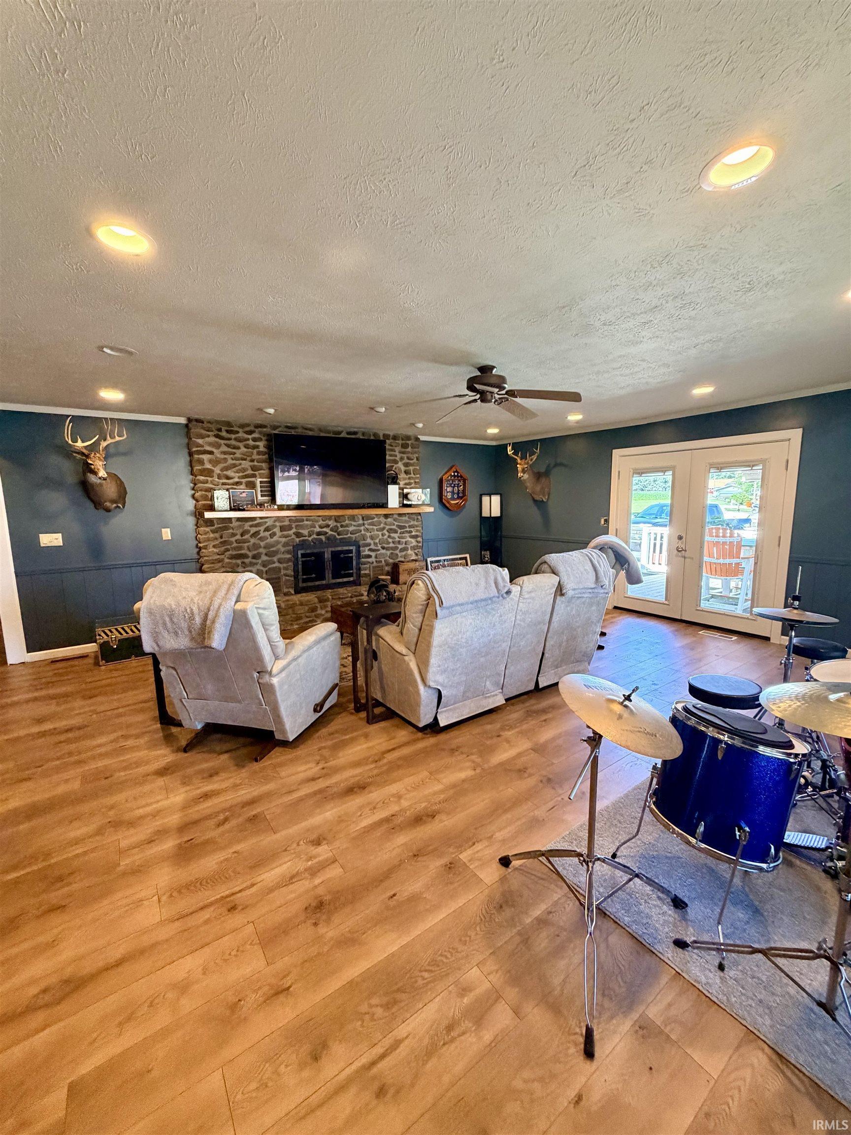 Image 2: Spacious living area featuring wood-finish flooring, a stone-faced fireplace with a wood mantel, and recessed ceiling lighting, Living Room