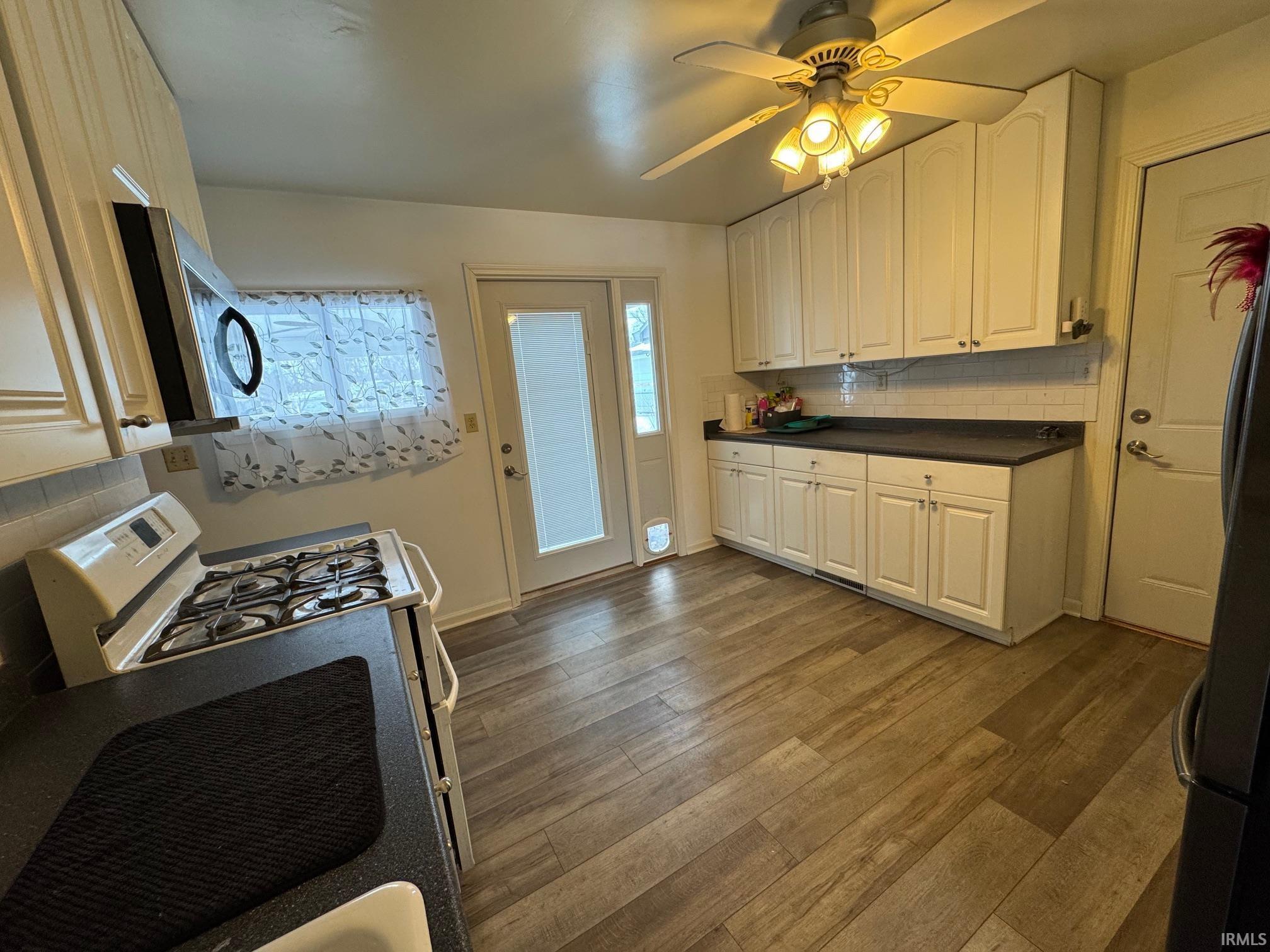 Image 2: Kitchen with decorative backsplash, dark countertops, stainless steel appliances, ceiling fan, and dark wood-style floors, Kitchen