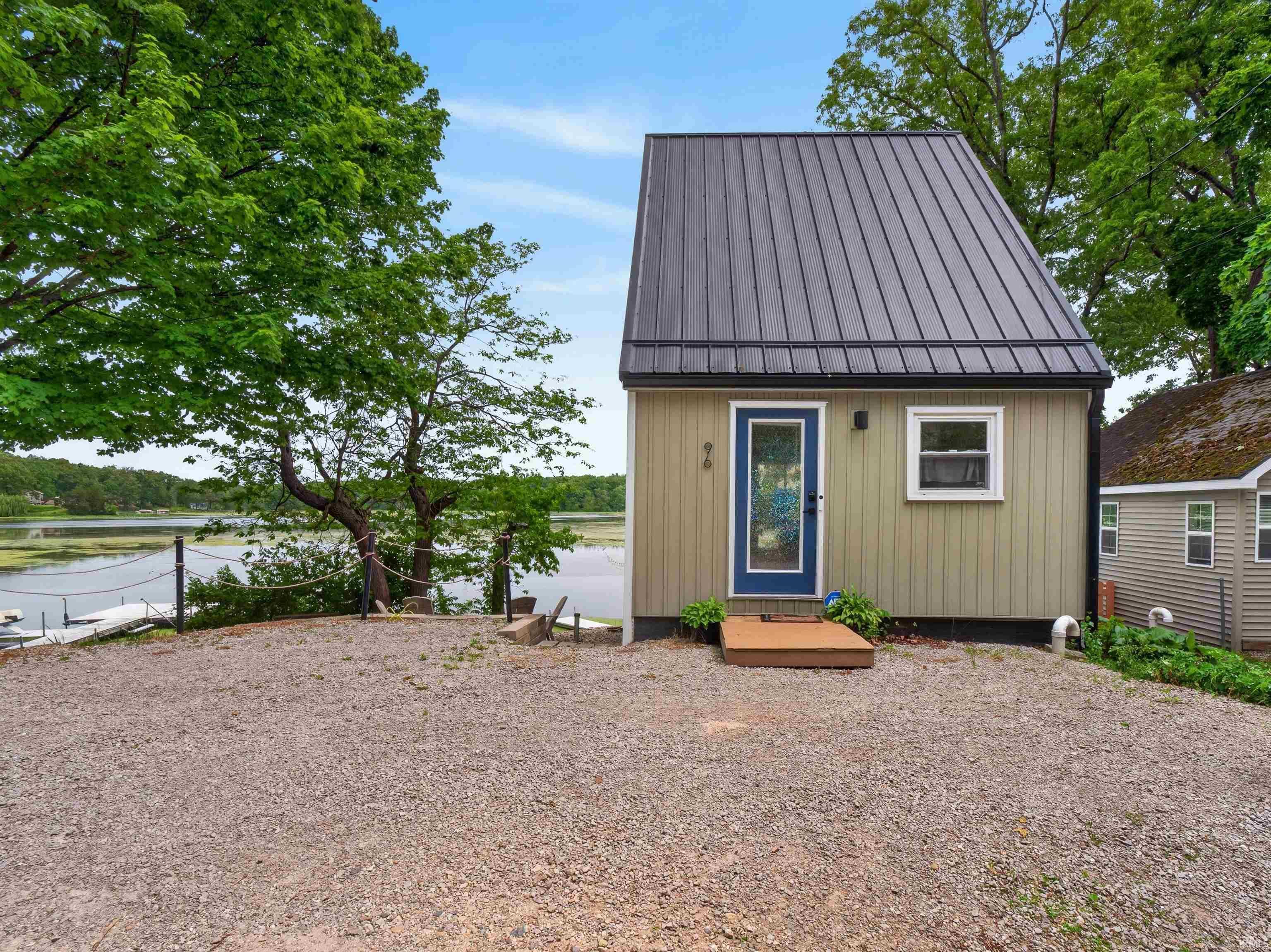 Image 1: Compact dwelling featuring a dark metal roof, light-colored vertical siding, and a blue entry door with a full-light panel, Front Of Structure Image 1: Compact dwelling featuring a dark metal roof, light-colored vertical siding, and a blue entry door with a full-light panel, Front Of Structure