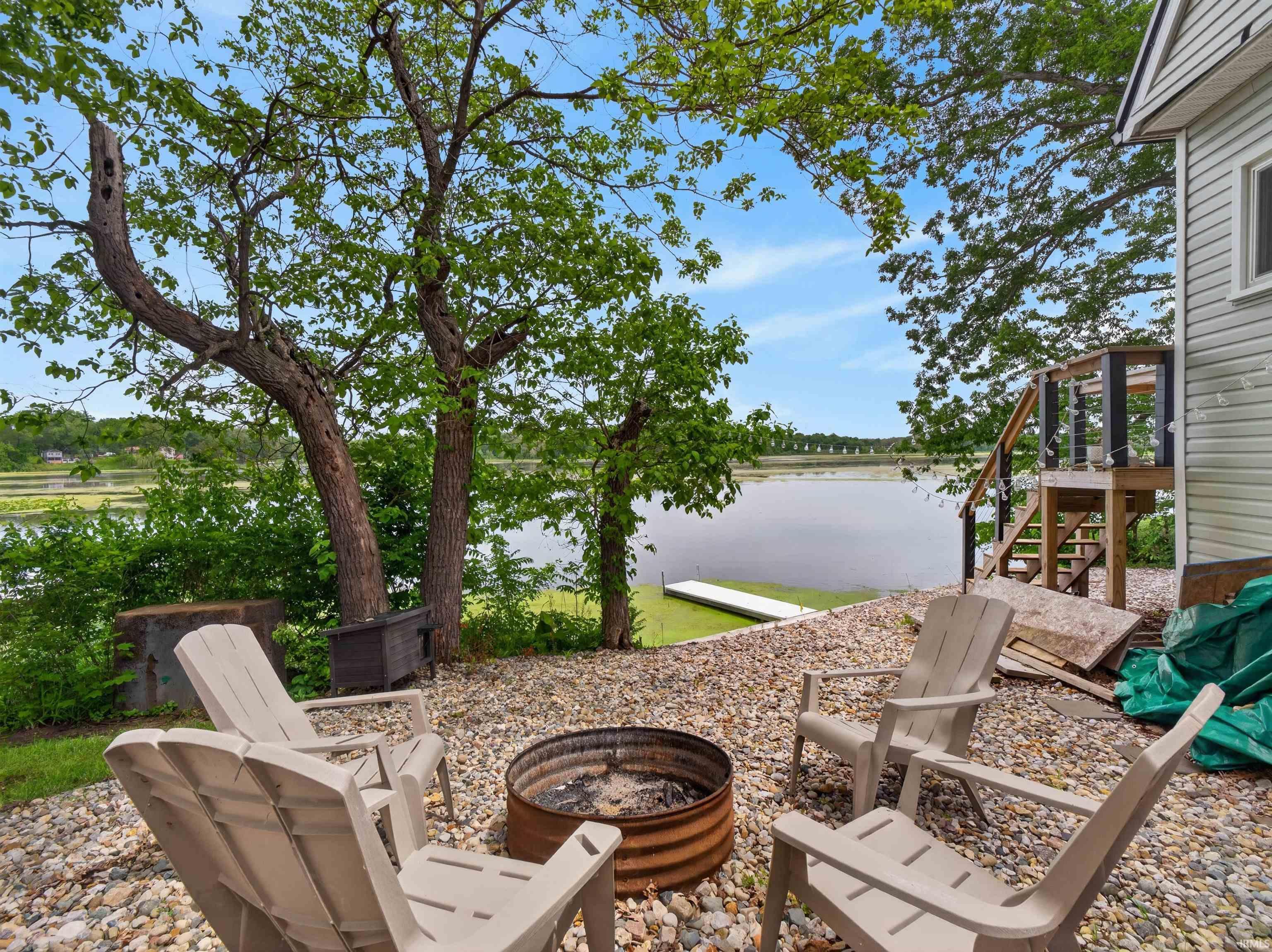 Image 2: Gravel patio area featuring a built-in fire pit, mature trees, and waterfront access with a dock, Patio Image 2: Gravel patio area featuring a built-in fire pit, mature trees, and waterfront access with a dock, Patio