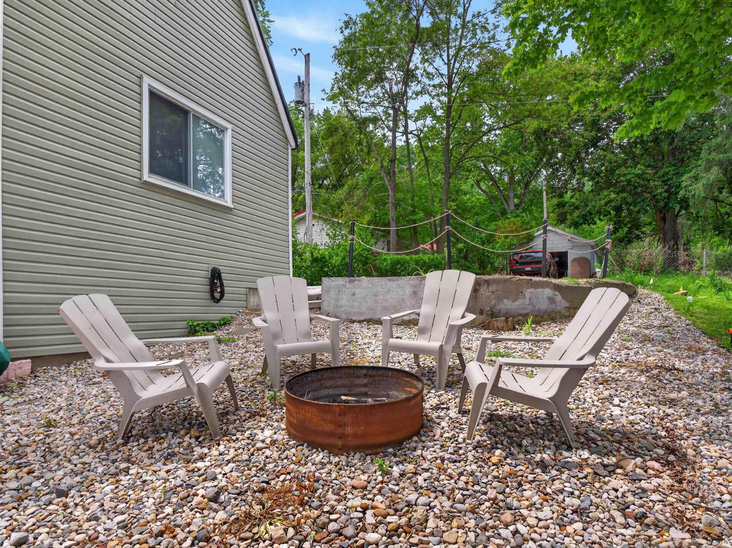 Image 3: Exterior side yard featuring a fire pit area with gravel ground cover, a utility shed, and mature perimeter trees, Patio Image 3: Exterior side yard featuring a fire pit area with gravel ground cover, a utility shed, and mature perimeter trees, Patio