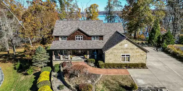 Image 2: Stone and wood-sided residence featuring a shingled roof, covered front porch, and mature landscaping, Front Of Structure Image 2: Stone and wood-sided residence featuring a shingled roof, covered front porch, and mature landscaping, Front Of Structure