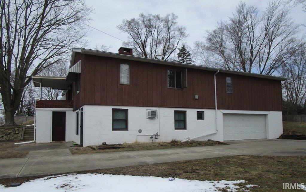 Image 1: Snow covered back of property featuring an attached garage, concrete driveway, and a chimney, Back Of Structure