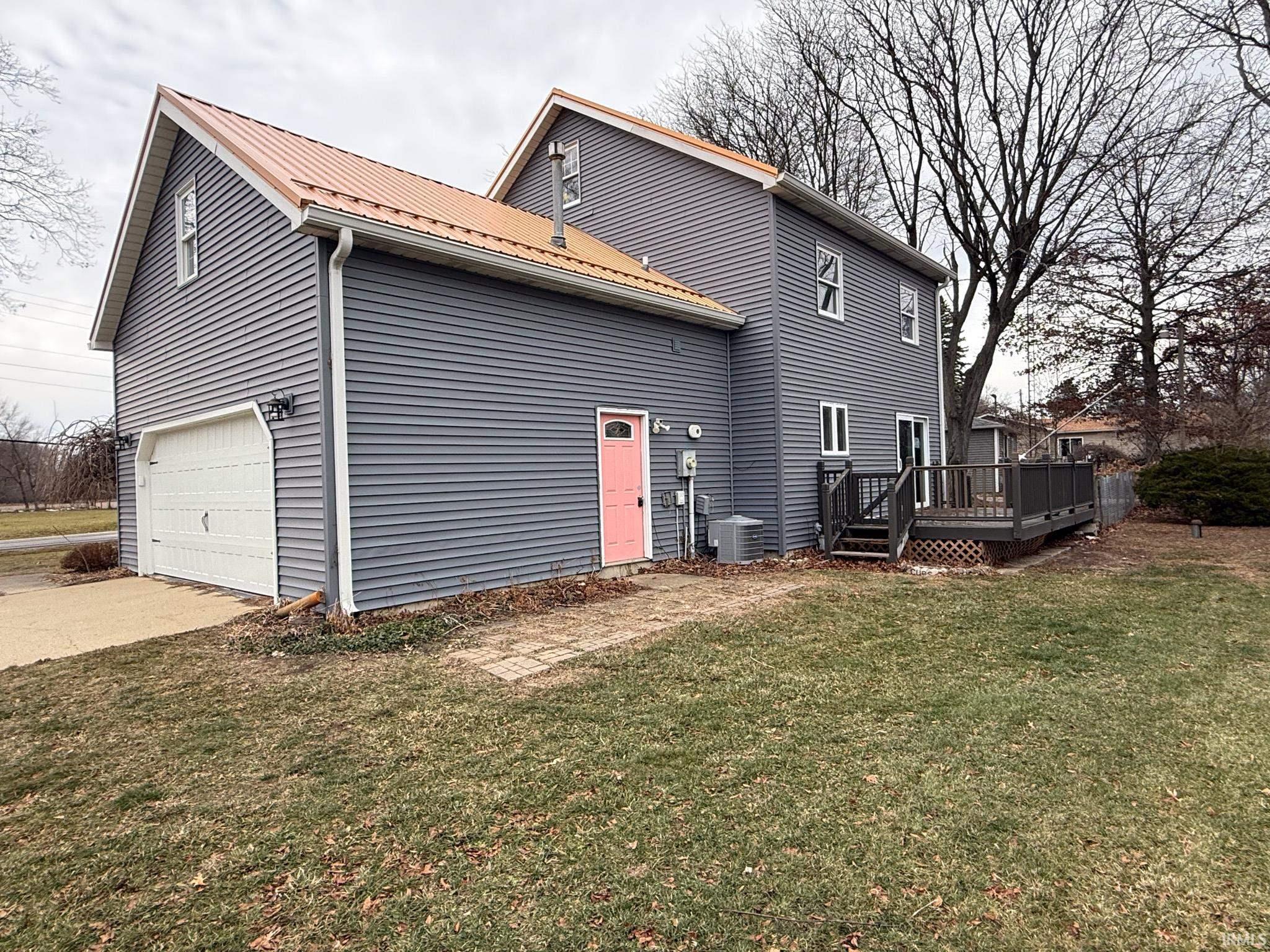 Image 0: Rear view of property featuring a lawn, concrete driveway, a wooden deck, a garage, and a metal roof, Back Of Structure Image 0: Rear view of property featuring a lawn, concrete driveway, a wooden deck, a garage, and a metal roof, Back Of Structure
