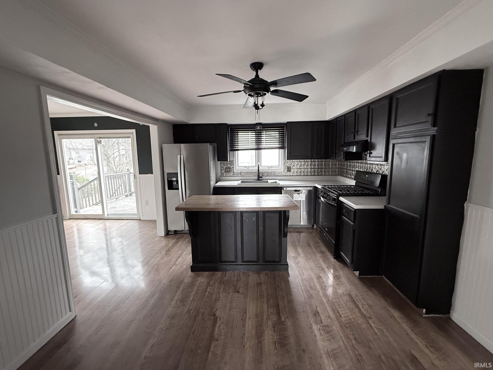 Image 1: Kitchen featuring a wainscoted wall, dark cabinets, stainless steel appliances, a center island, and ceiling fan, Kitchen Image 1: Kitchen featuring a wainscoted wall, dark cabinets, stainless steel appliances, a center island, and ceiling fan, Kitchen