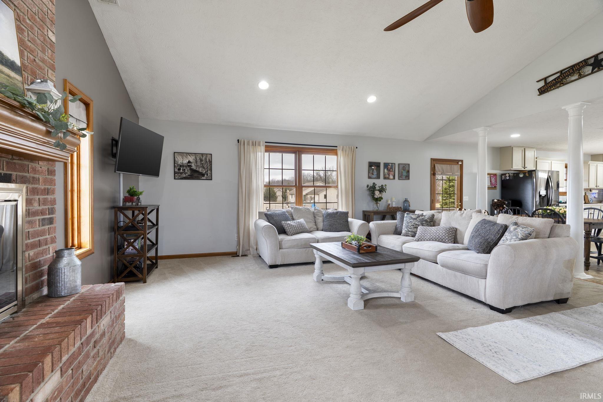 Image 3: Living area featuring lofted ceiling, a brick fireplace, light colored carpet, a ceiling fan, and ornate columns, Living Room
