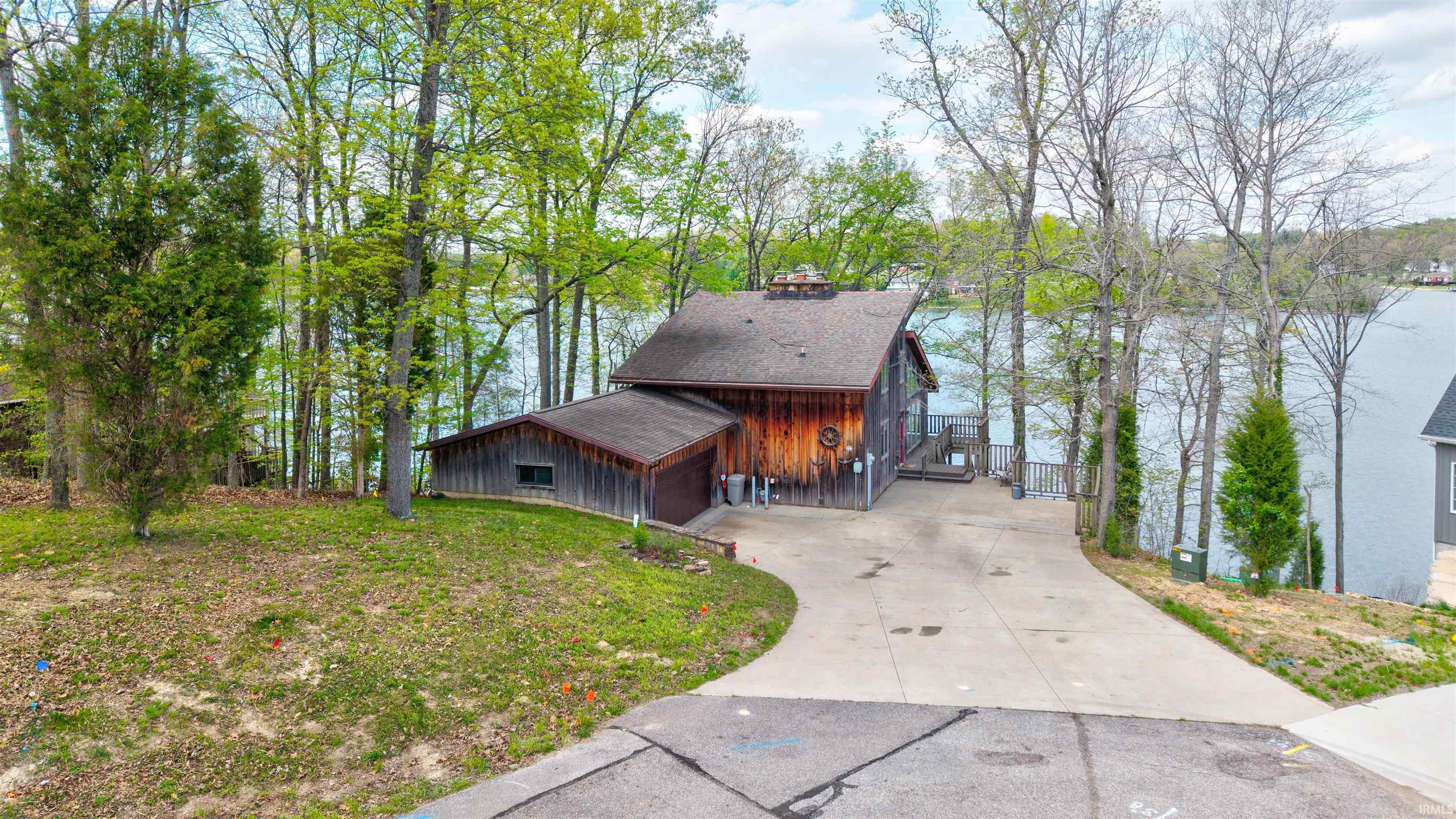 Image 0: View of front of property featuring a garage, concrete driveway, a front lawn, a chimney, and a water view, Front Of Structure Image 0: View of front of property featuring a garage, concrete driveway, a front lawn, a chimney, and a water view, Front Of Structure