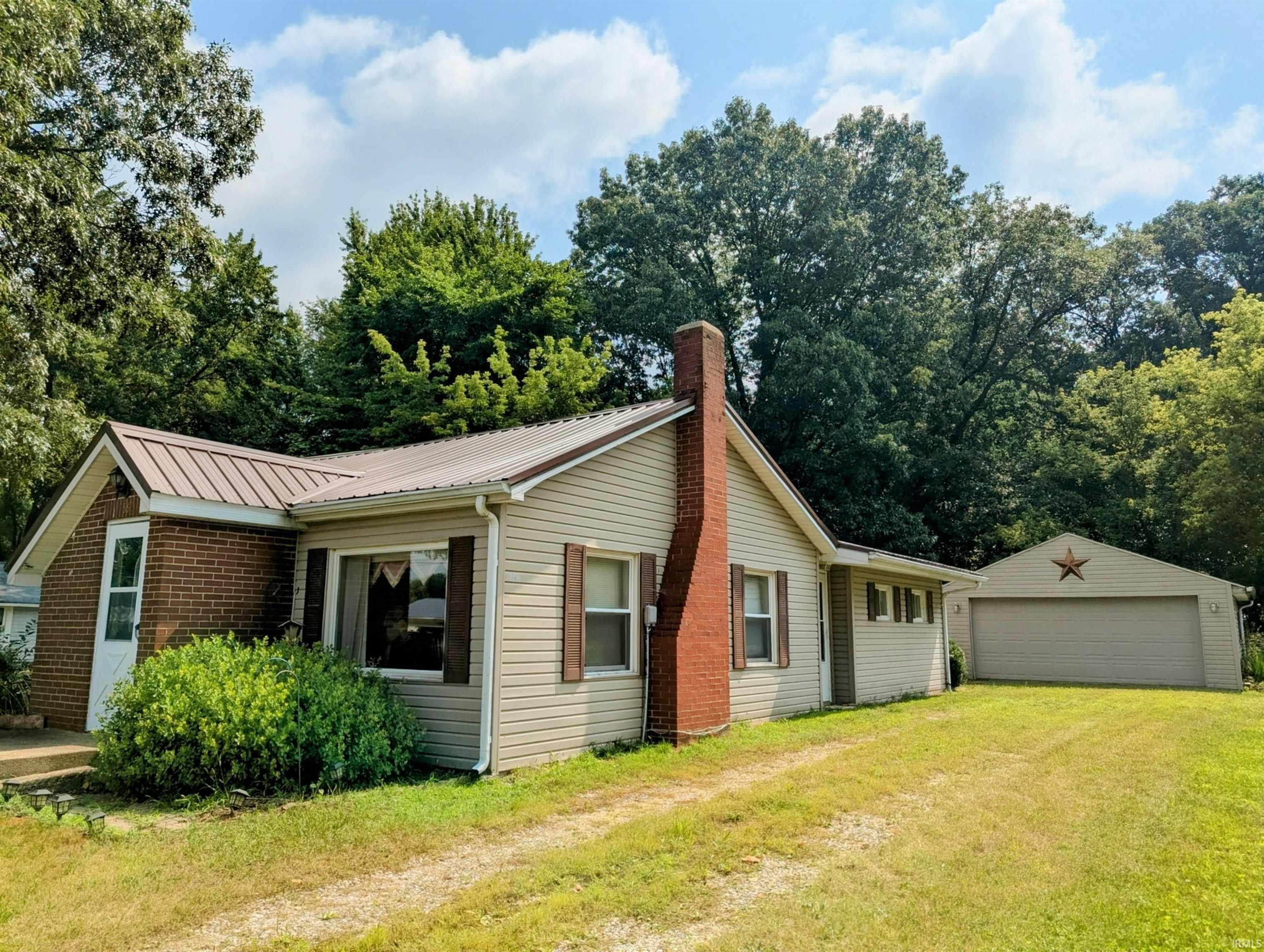 Image 0: Single-story residence featuring light-toned siding, a brown metal roof, and a prominent brick chimney, Front Of Structure Image 0: Single-story residence featuring light-toned siding, a brown metal roof, and a prominent brick chimney, Front Of Structure