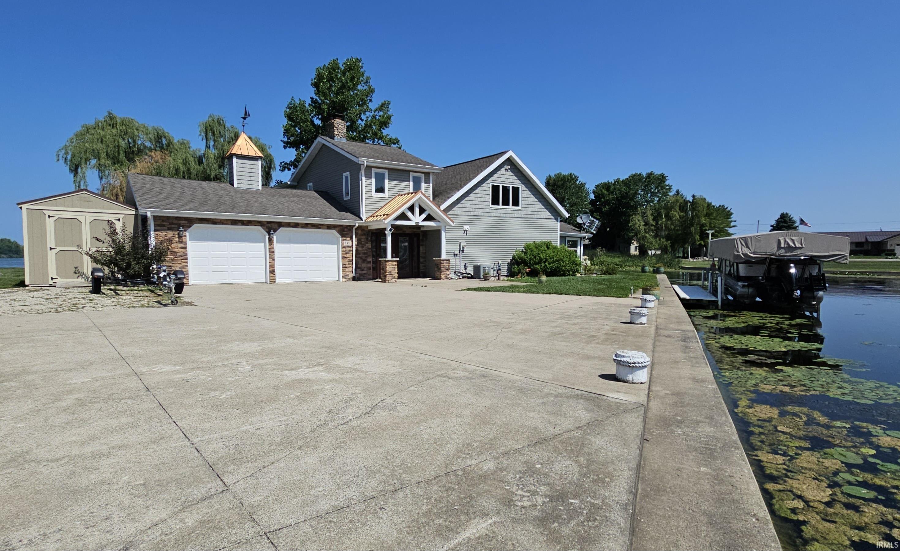 Image 1: View of front facade featuring a garage, driveway, a chimney, a water view, and a storage shed, Front Of Structure