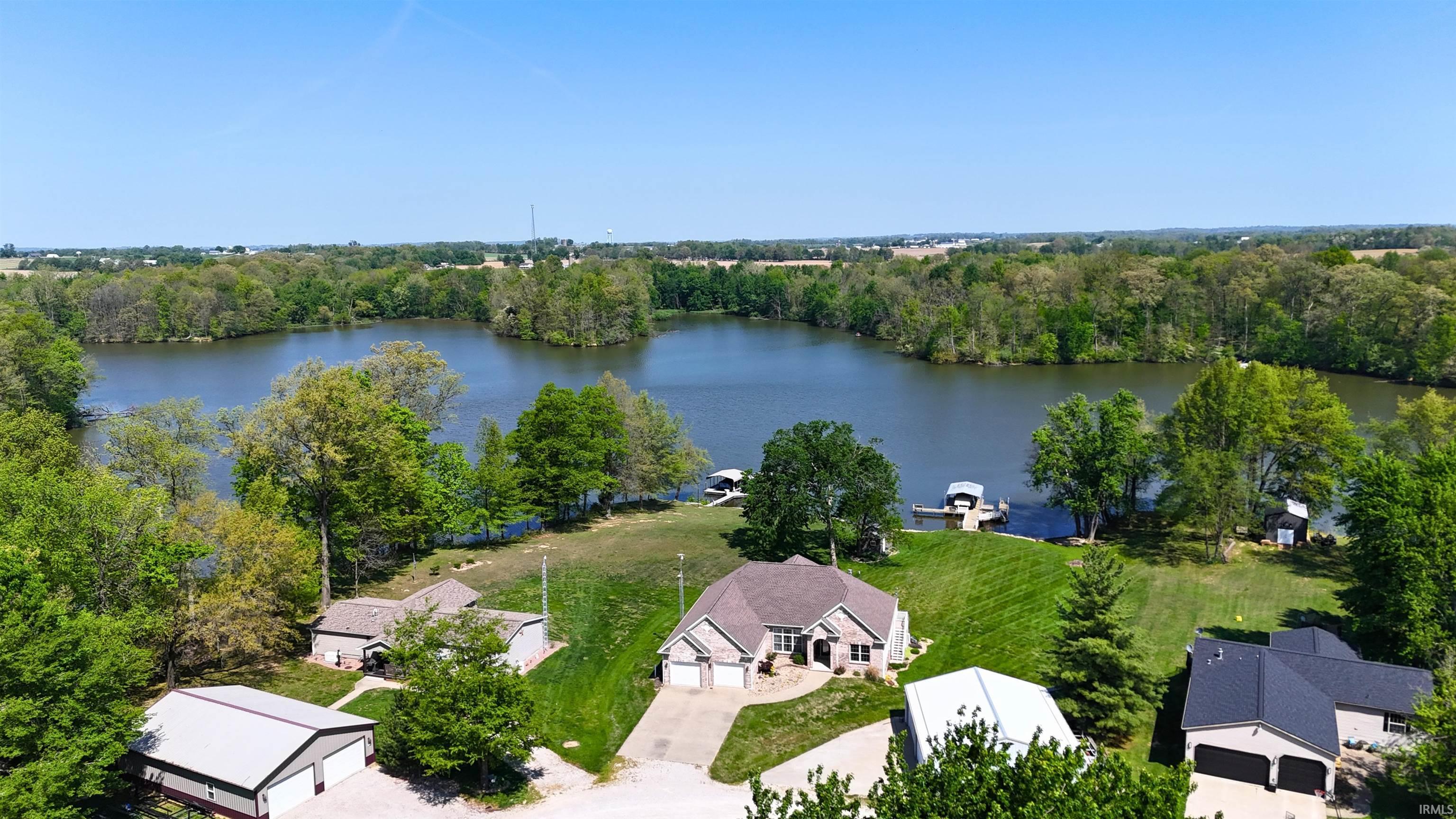 Image 1: Expansive waterfront property featuring a gently sloped lawn to the water's edge, a private boat dock with two covered slips, mature perimeter trees, and a spacious single-story residence with an attached two-car garage, Aerial View