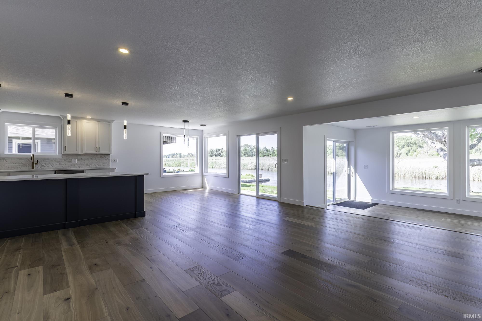 Image 2: Open-concept living area with wood-finish flooring, a kitchen island with dark cabinetry, white perimeter cabinetry, multiple pendant lights, and numerous windows and glass doors offering abundant natural light, Living Room