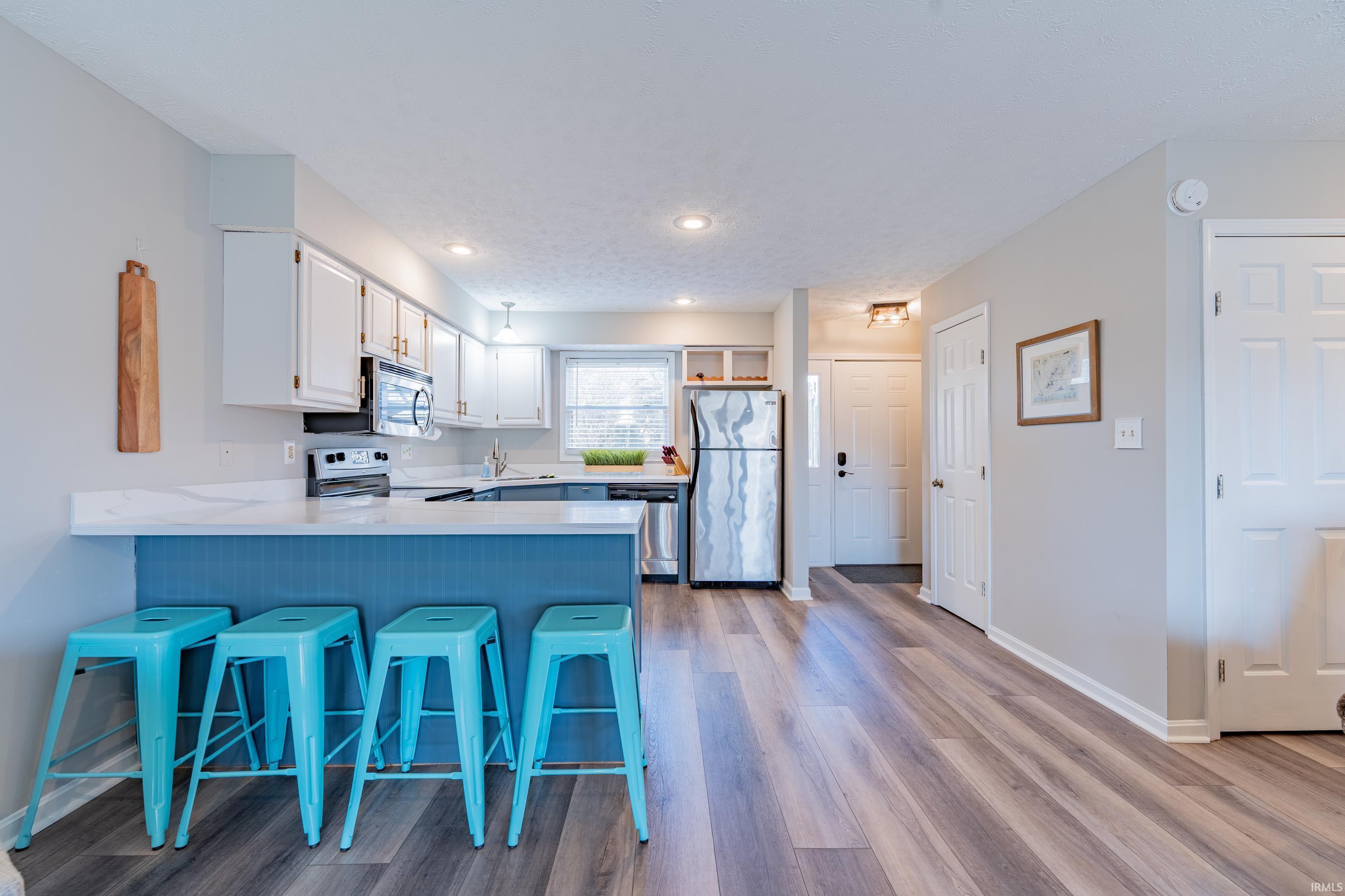 Image 3: Kitchen featuring a breakfast bar area, a peninsula, stainless steel appliances, white cabinetry, and light wood-type flooring, Kitchen Image 3: Kitchen featuring a breakfast bar area, a peninsula, stainless steel appliances, white cabinetry, and light wood-type flooring, Kitchen