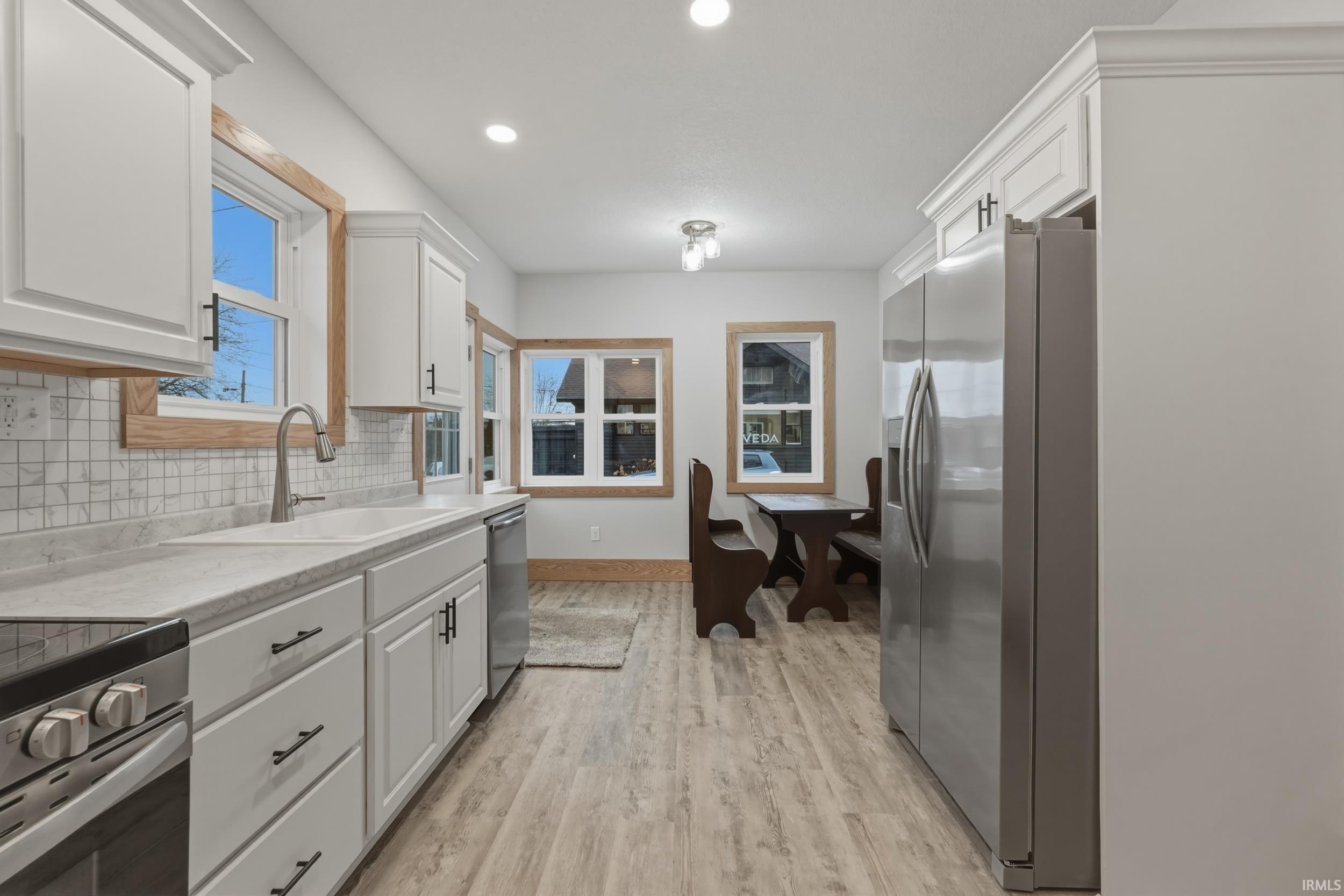 Image 3: Kitchen with stainless steel appliances, white cabinetry, light wood finished floors, recessed lighting, and backsplash, Kitchen