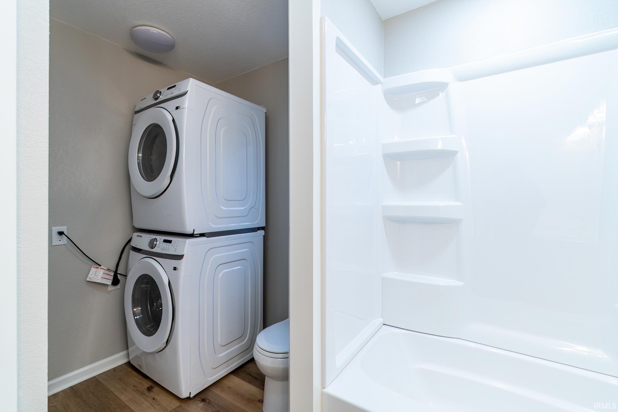 Image 3: Full bath featuring stacked washer / drying machine, wood finished floors, and a shower, Laundry Bathroom