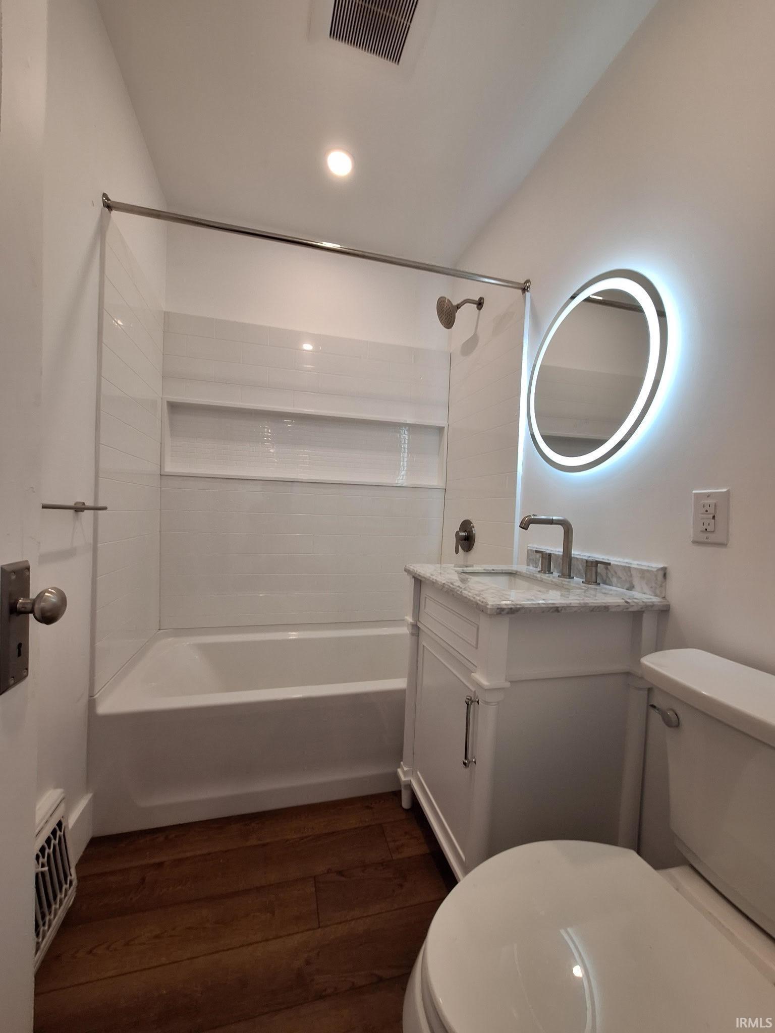 Image 2: White vanity with stone countertop and undermount sink, illuminated mirror, chrome fixtures, and wood-finish flooring, Bathroom Image 2: White vanity with stone countertop and undermount sink, illuminated mirror, chrome fixtures, and wood-finish flooring, Bathroom