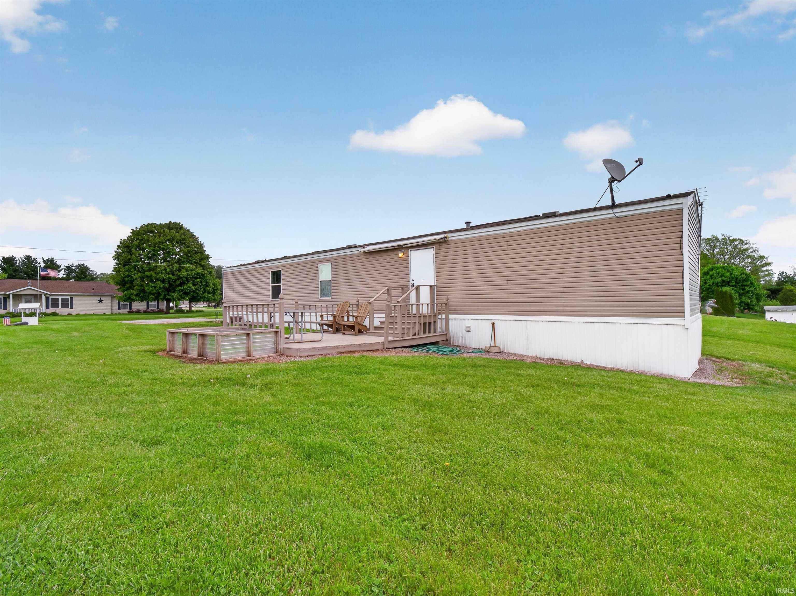 Image 2: Expansive green lawn surrounds the property, featuring a raised deck with wood railing, Back Of Structure